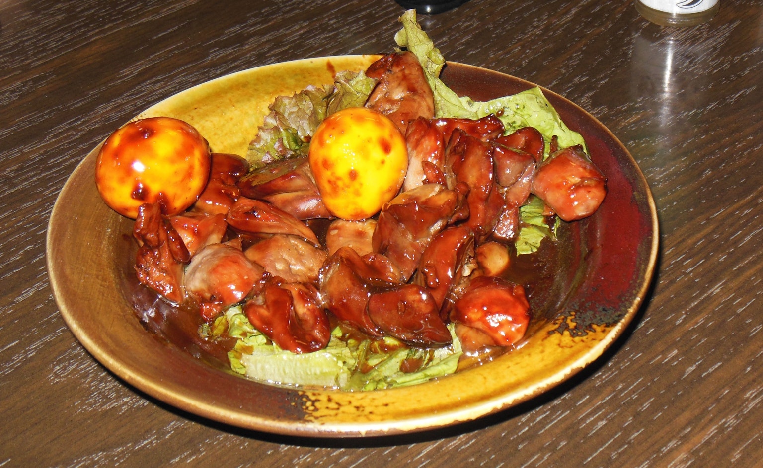 A plate of chicken and eggs dish fresh lettuce and rich sauce