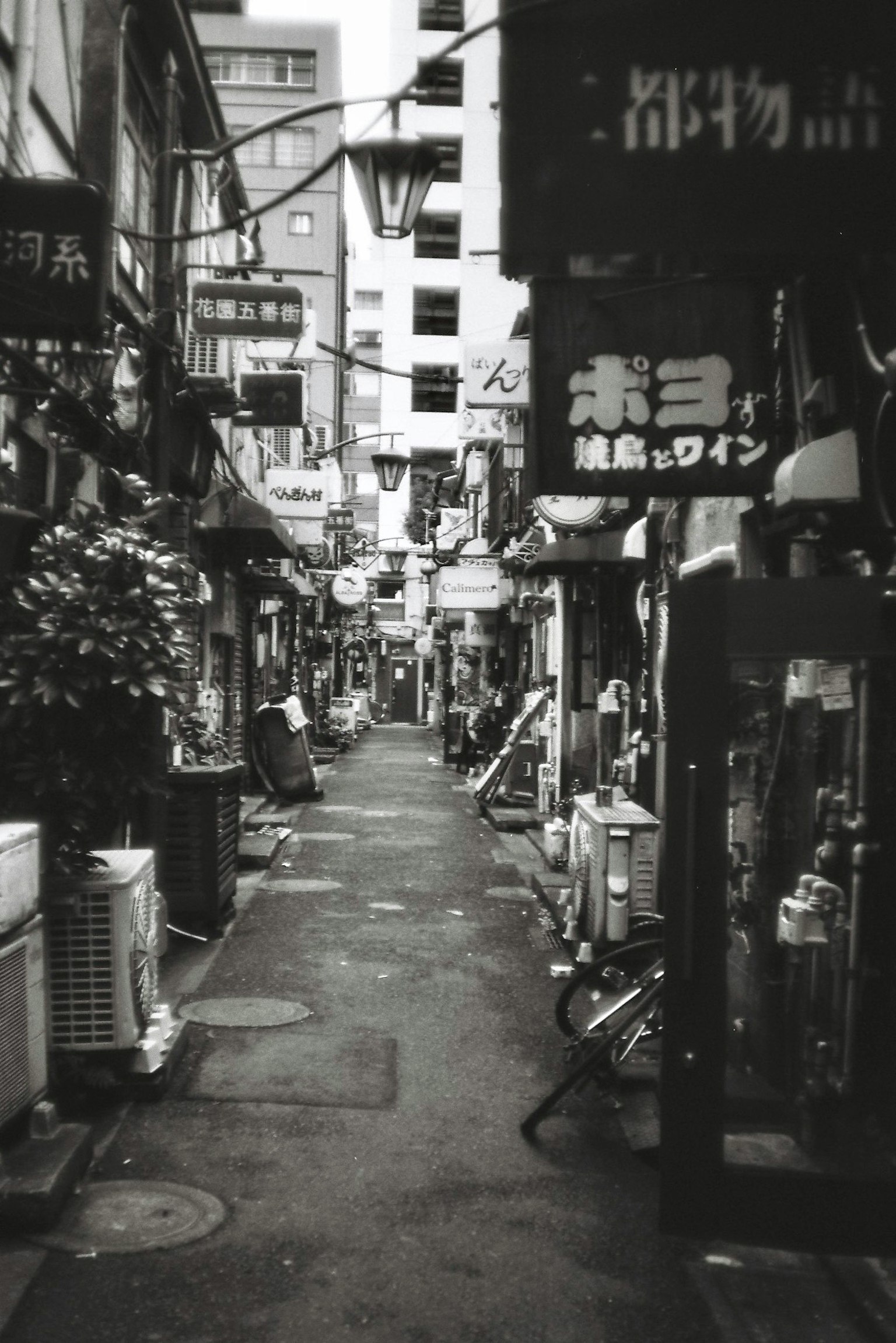 Callejón estrecho en blanco y negro en Japón con varios letreros y tiendas