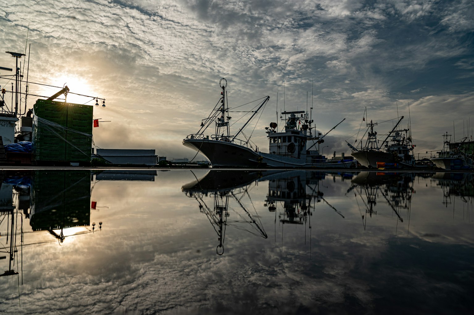 Silueta de barcos en un puerto tranquilo reflejándose en el agua y el cielo