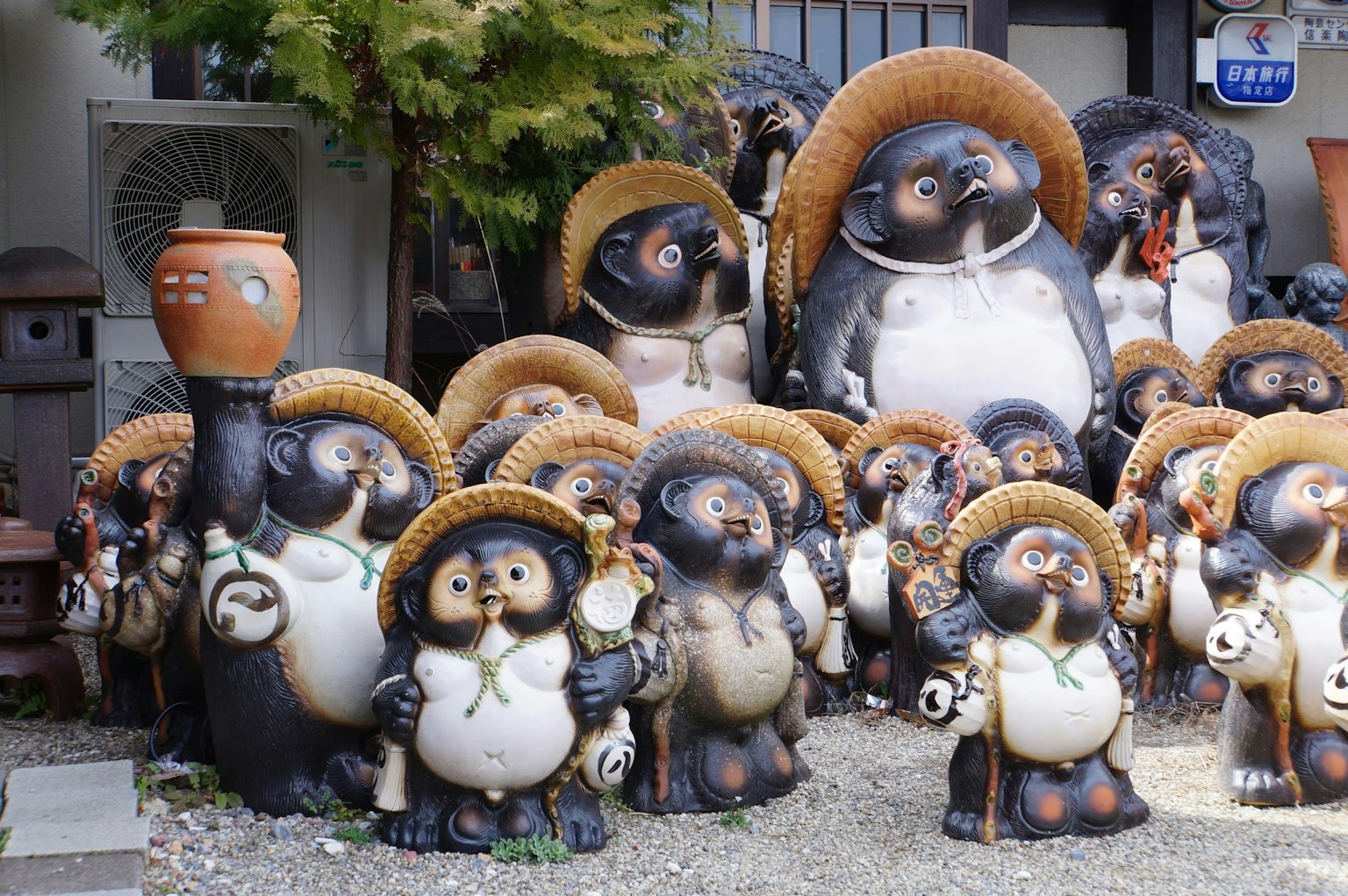 Una colección de figuras de tanuki de cerámica con sombreros de paja expuestas al aire libre
