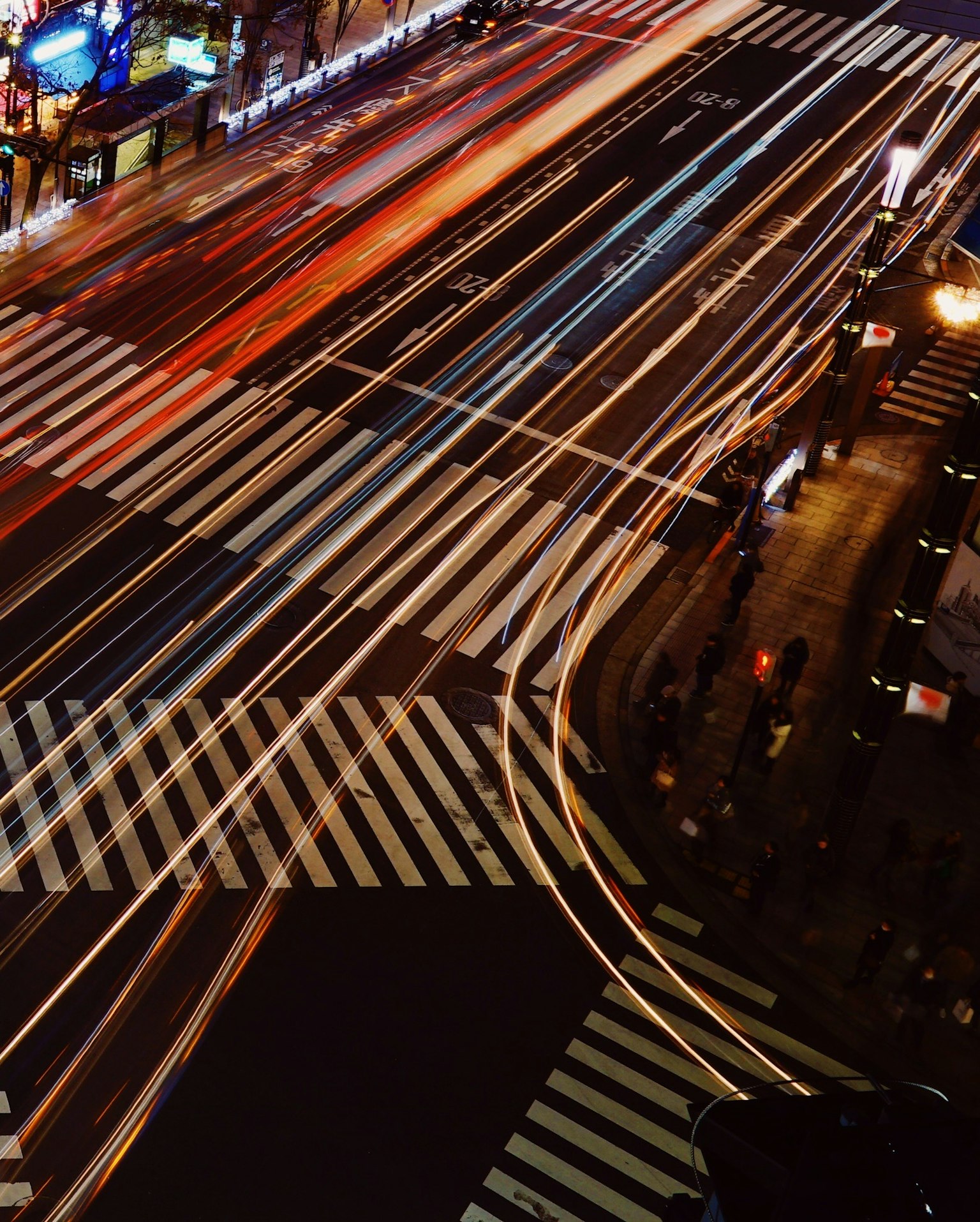 Luftaufnahme einer belebten Kreuzung mit Lichtspuren von Fahrzeugen und Fußgängern bei Nacht