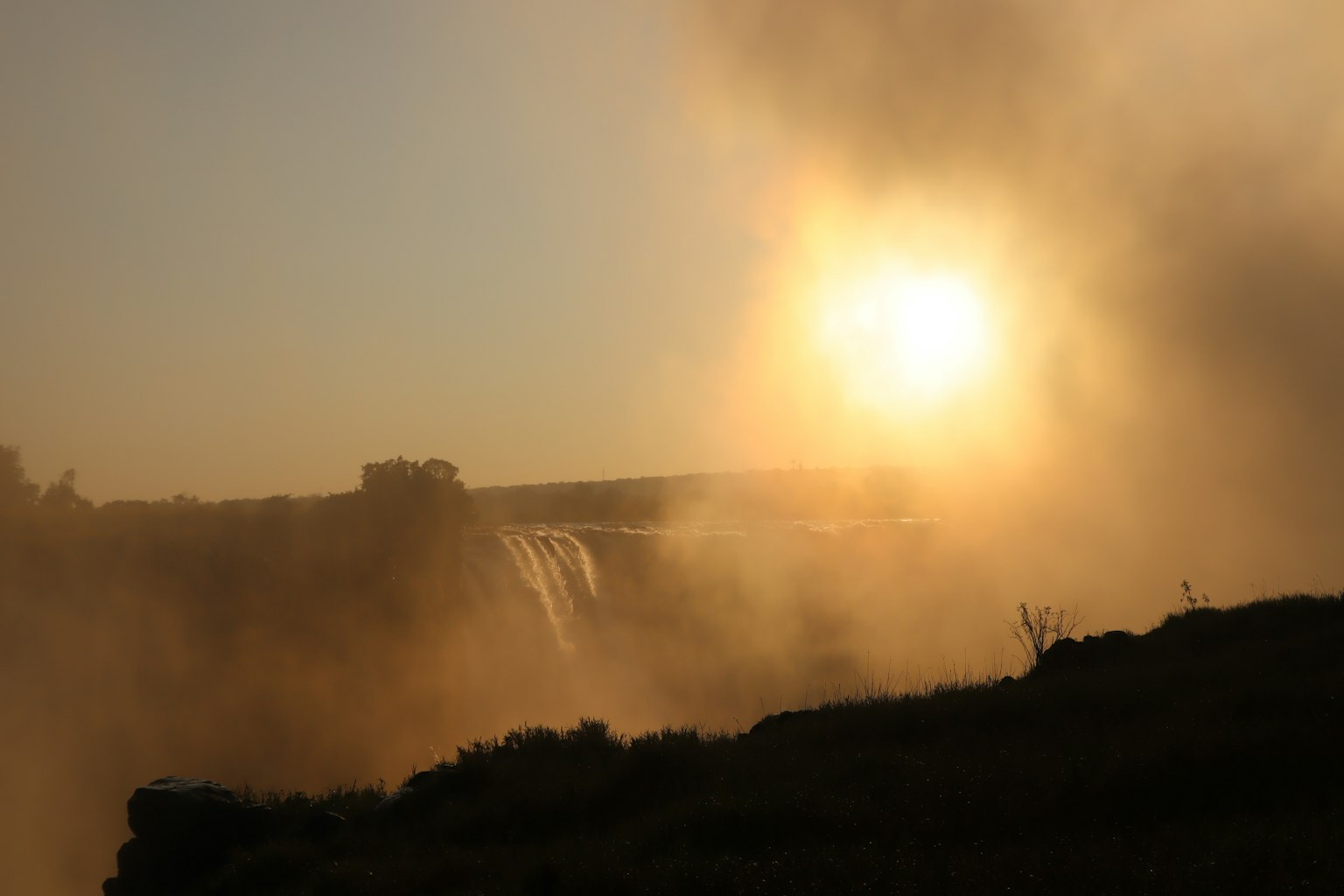 Silhouette di una cascata e di un tramonto avvolti nella nebbia