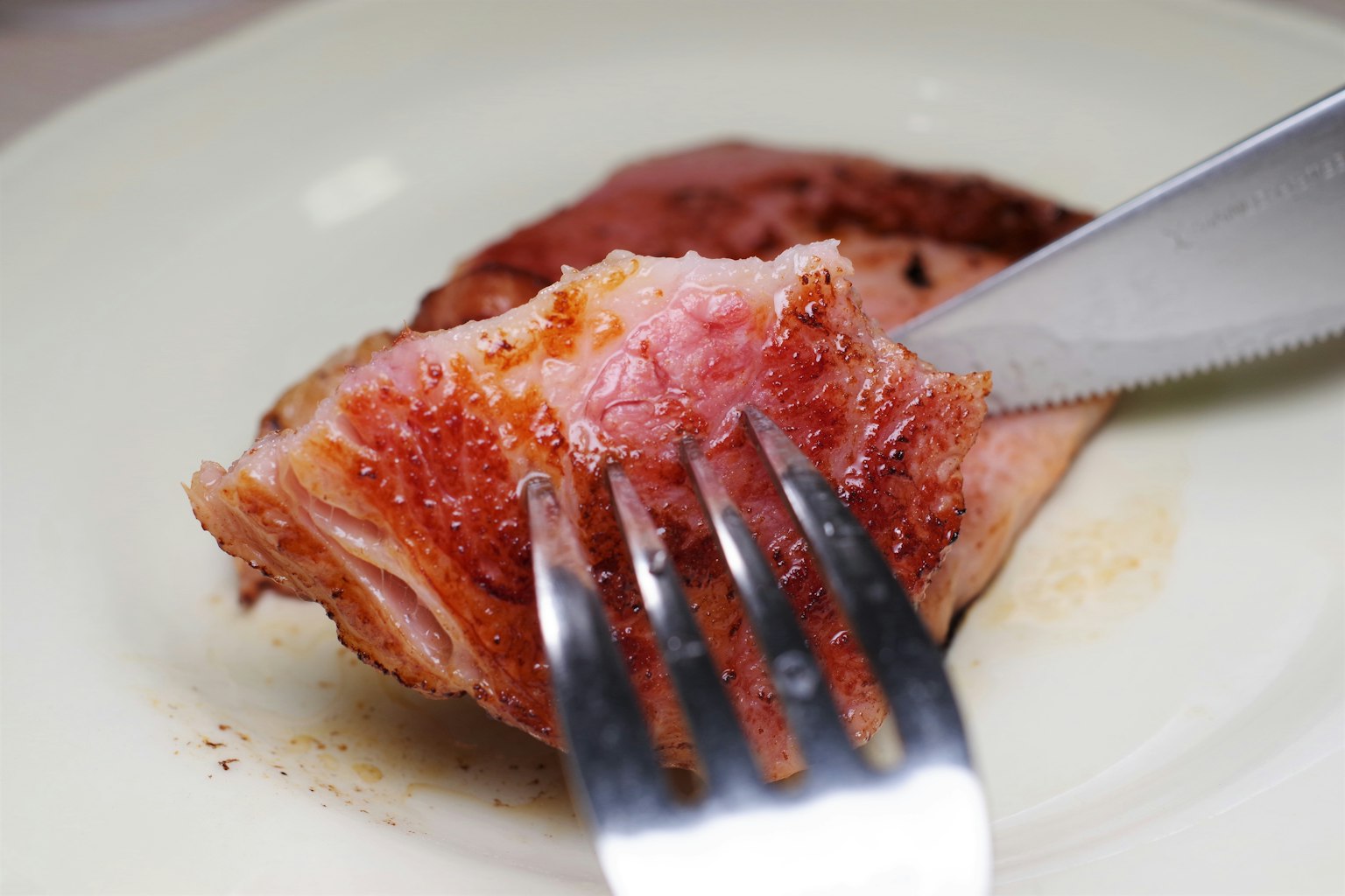 Ein Stück gegrilltes Fleisch auf einem Teller mit einer Gabel und einem Messer, das hineinschneidet