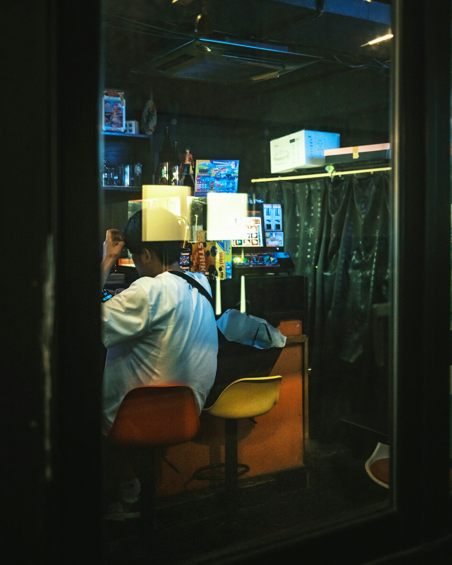 Blick durch ein Fenster auf das Innere eines Cafés mit einer sitzenden Person und bunten Stühlen