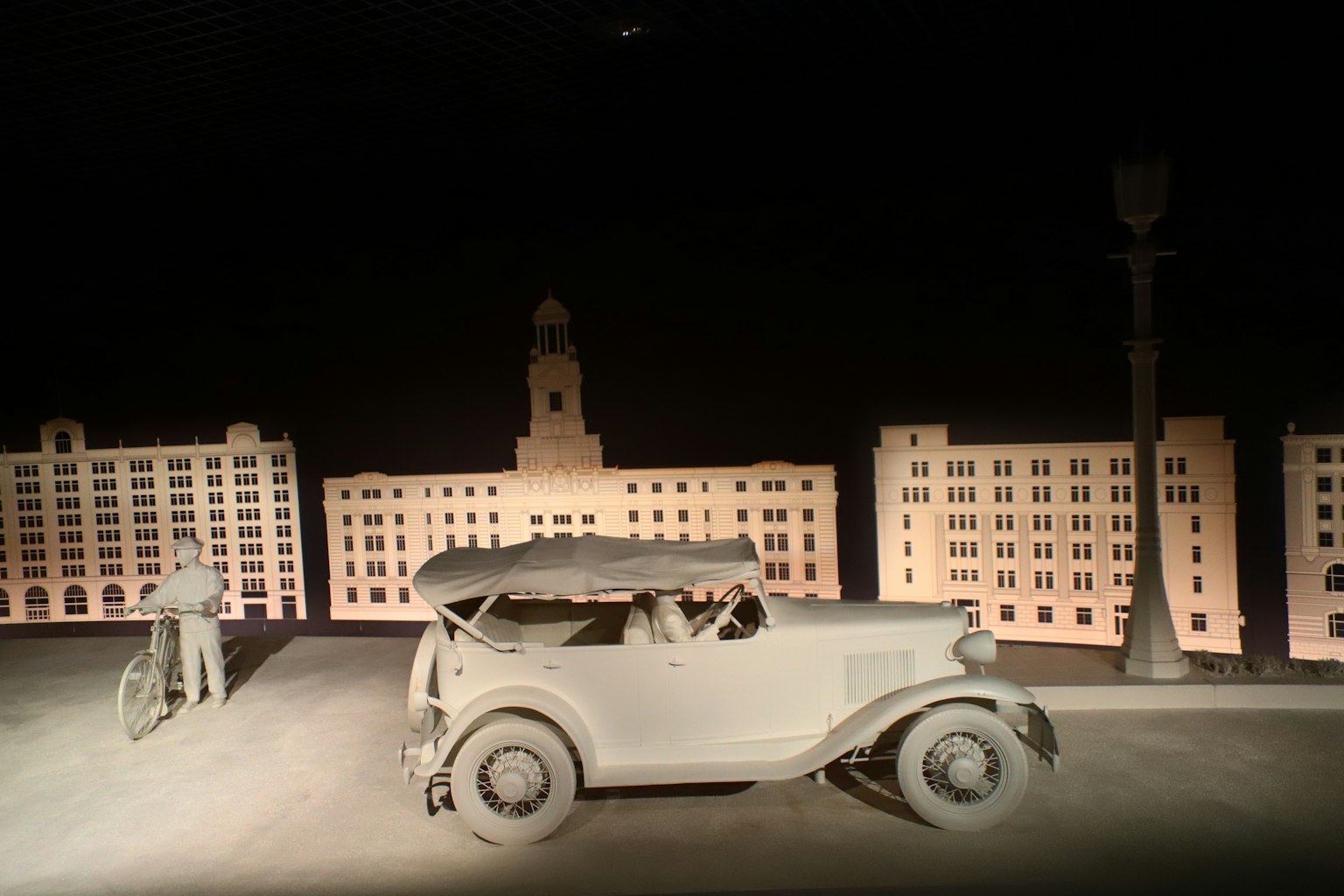 Auto monocromatica degli anni 1920 e sculture di persone in un paesaggio urbano