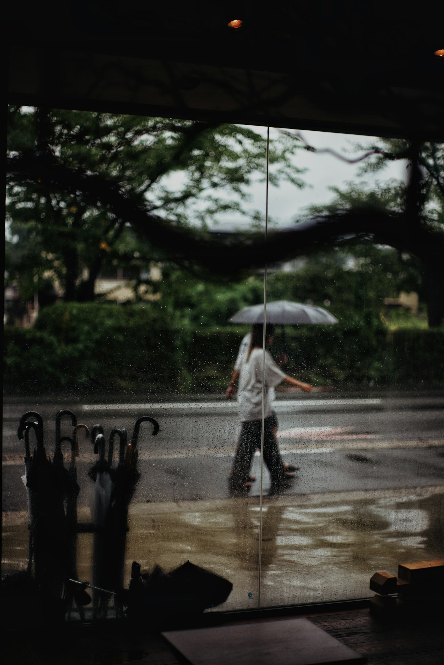 Una persona caminando con un paraguas bajo la lluvia vista a través de una ventana