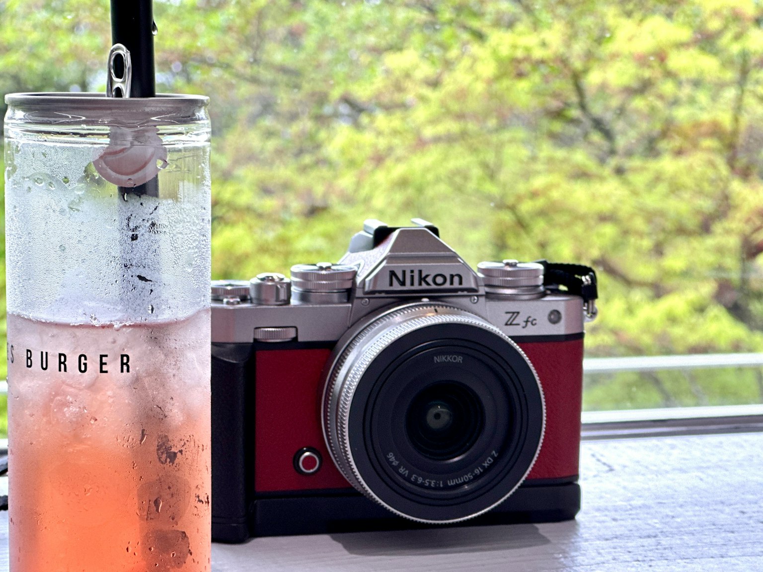 Un appareil photo Nikon Z9 rouge à côté d'un verre de boisson rose sur une table