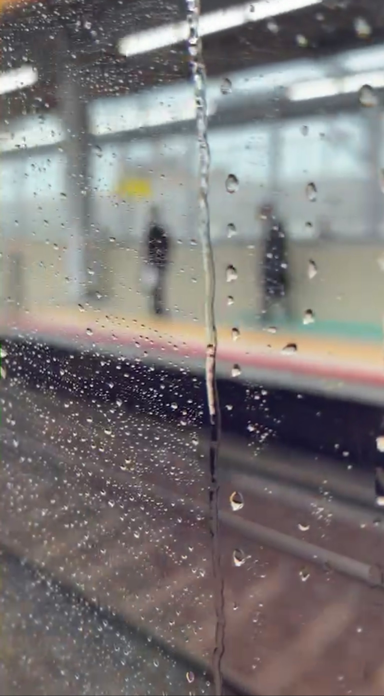 火车窗户上有雨滴显示模糊的平台和等待乘客的轮廓