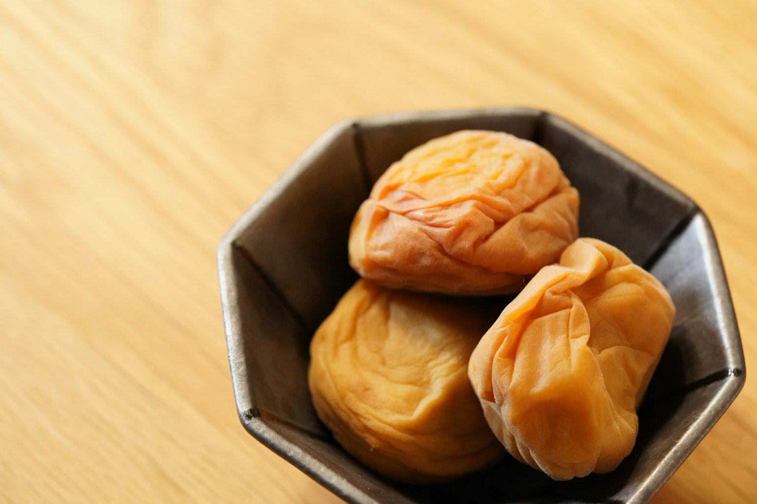 Plum kering dalam mangkuk hitam kecil di permukaan kayu
