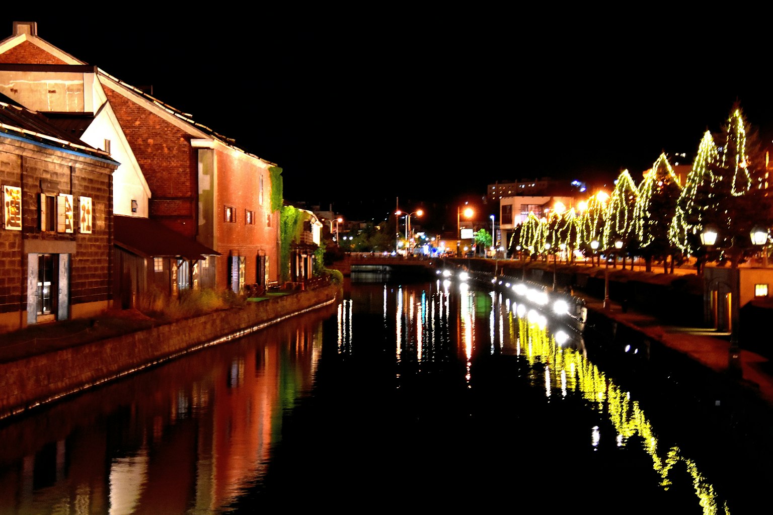 Vista nocturna de un canal con árboles iluminados y edificios reflejados en el agua