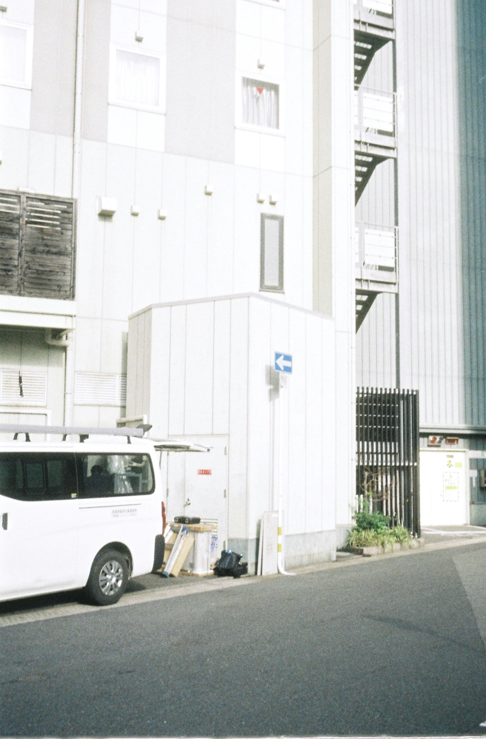 白いビルの路地に停まるバンと街灯