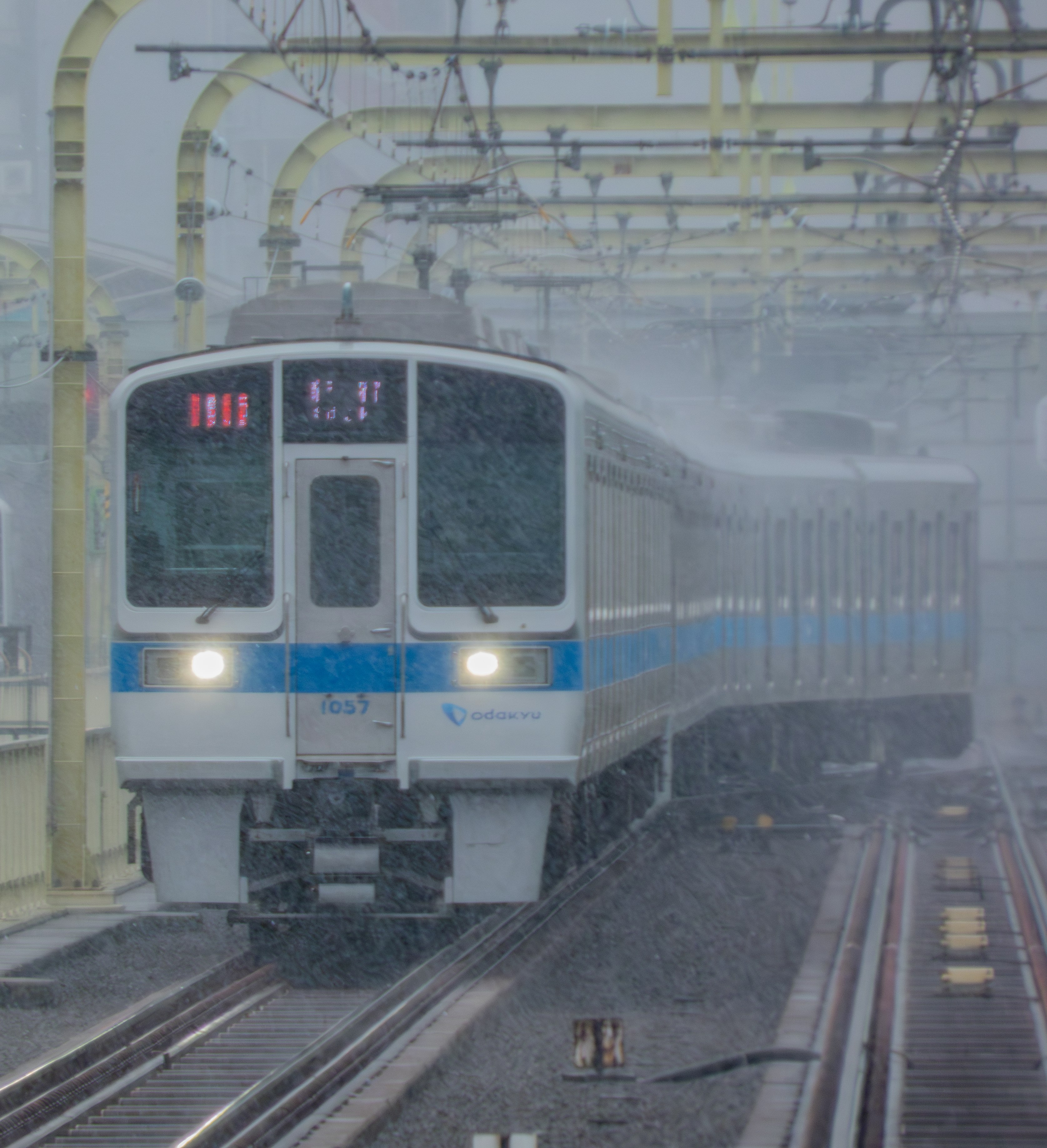 土砂降りの雨の中、線路を転線する小田急1000形電車の前面