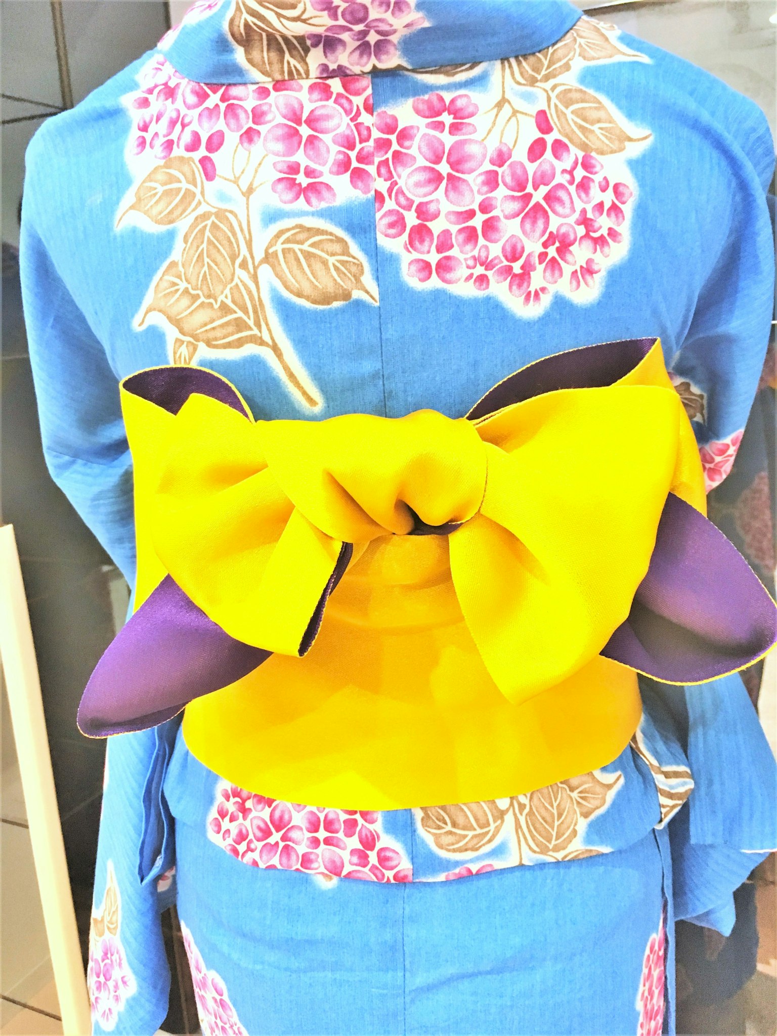 Tampilan belakang kimono biru dengan obi kuning besar terikat