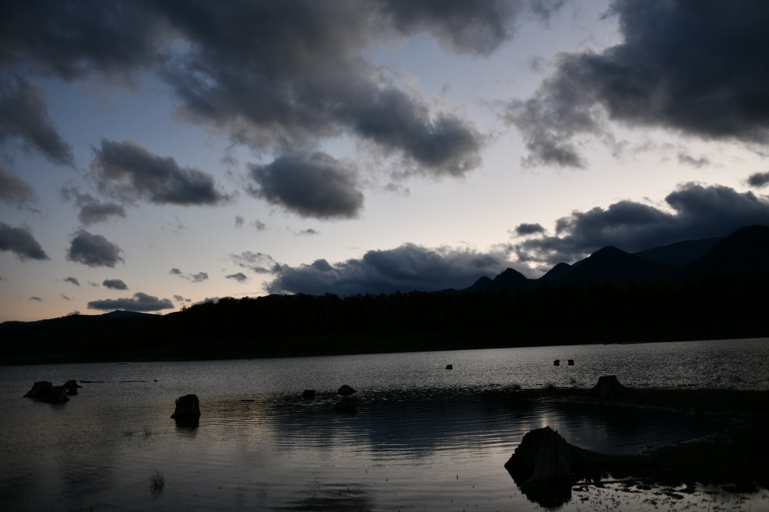 Silhouette gunung dan danau saat senja dengan awan dramatis