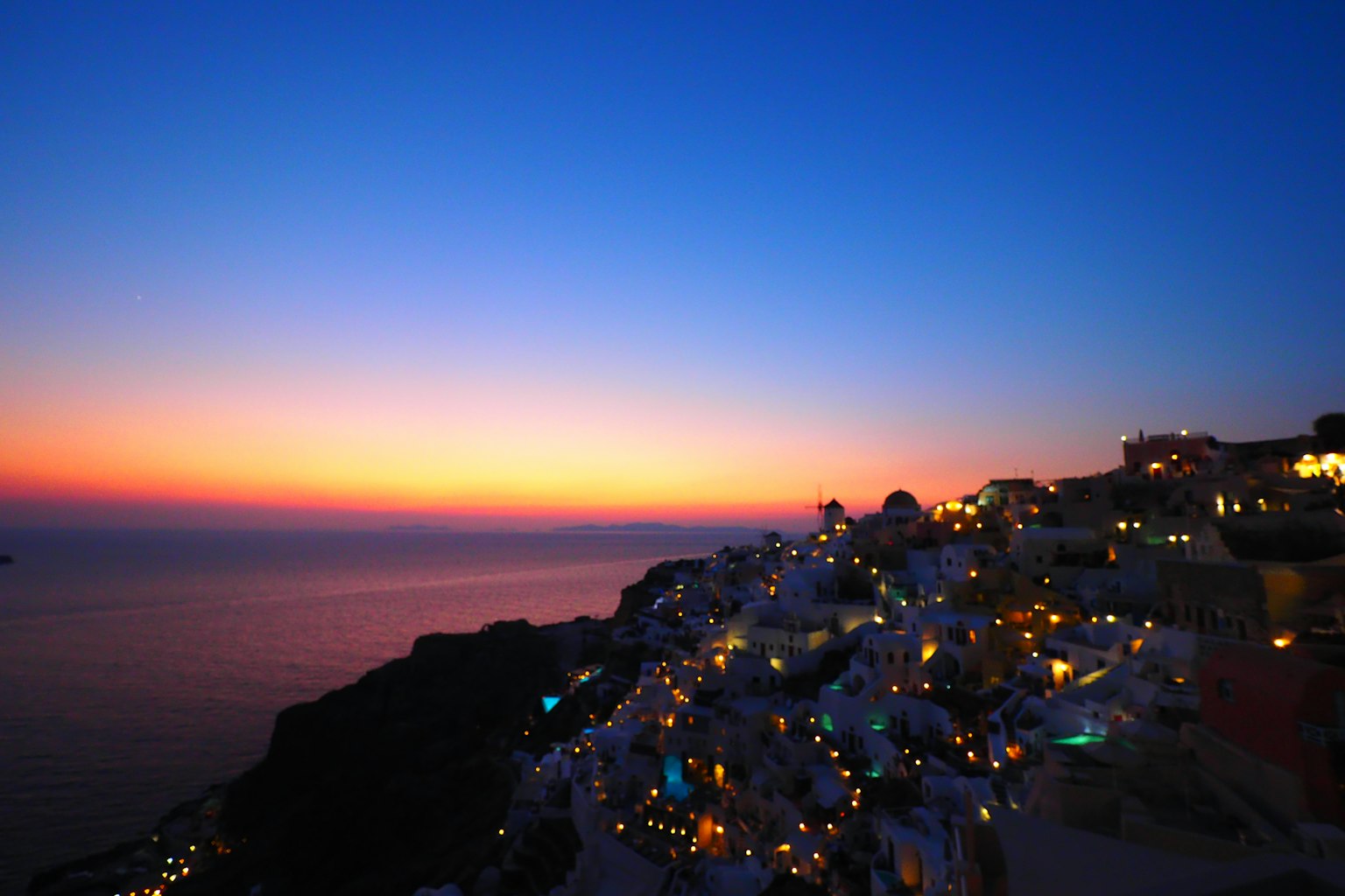 Cảnh hoàng hôn tuyệt đẹp ở Santorini với biển và ánh đèn từ những ngôi nhà trắng
