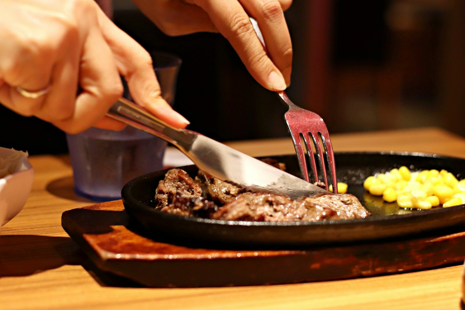 Manos cortando un filete en un plato caliente con maíz