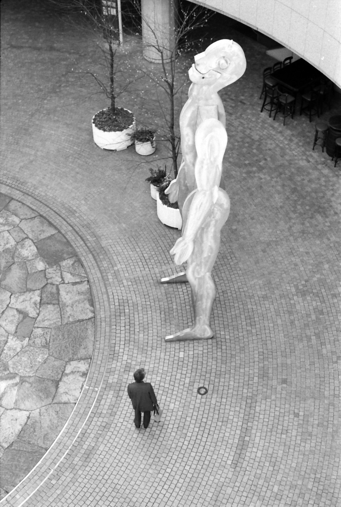escena en blanco y negro en un patio con figura escultórica y una persona caminando
