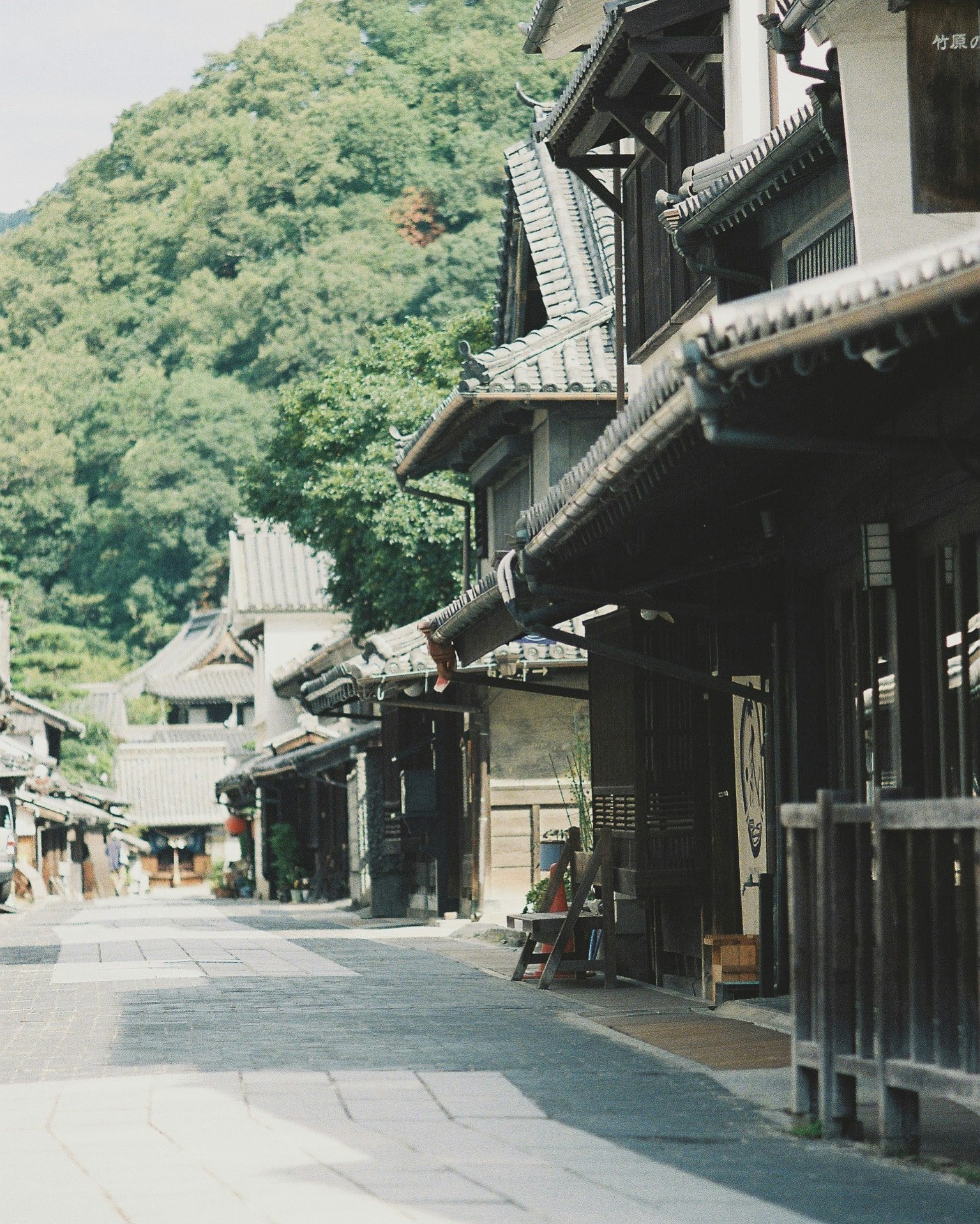 緑の山を背景にした古い町並みの路地と木造の軒先