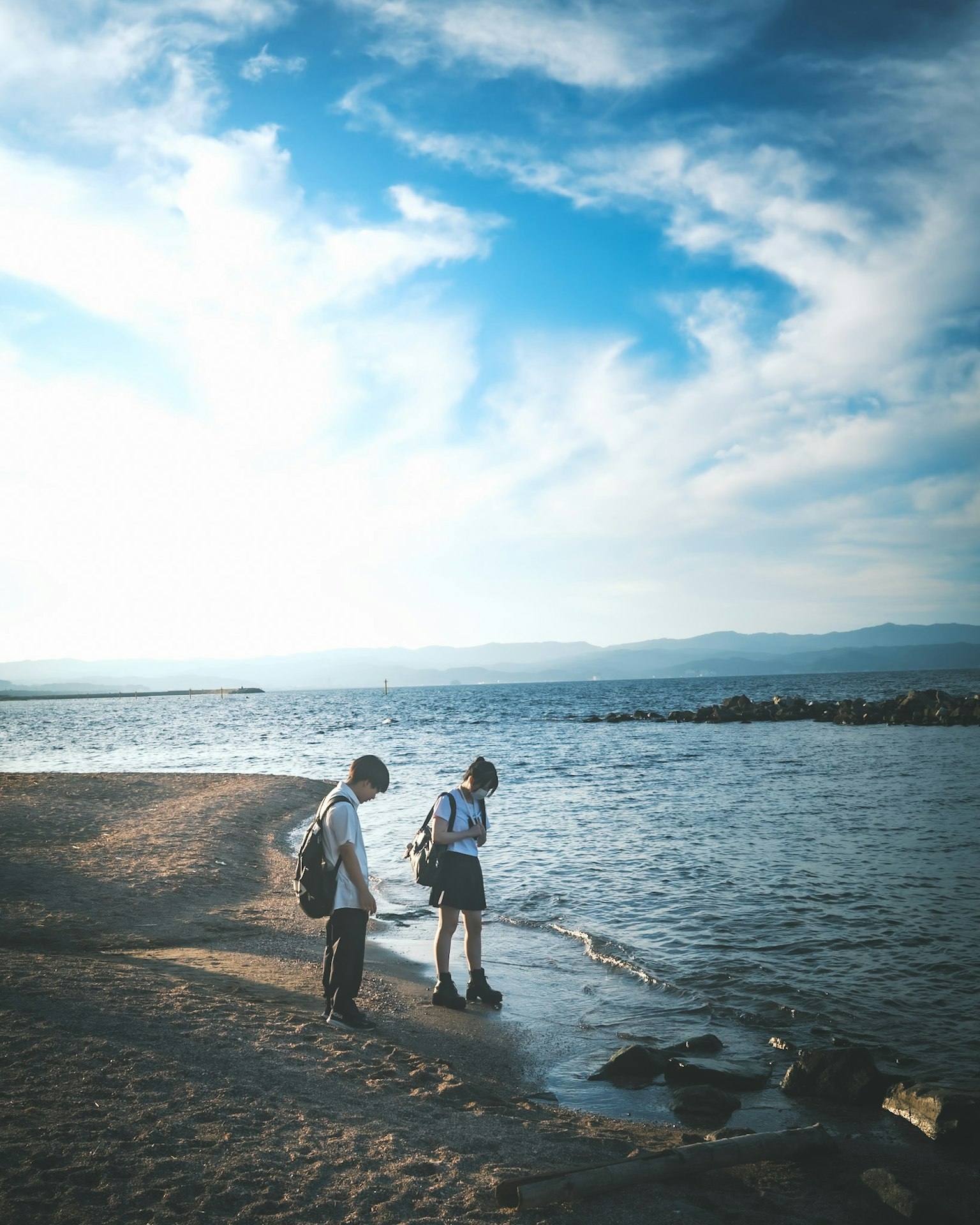两个人在海滩上沿着水边走，蓝天