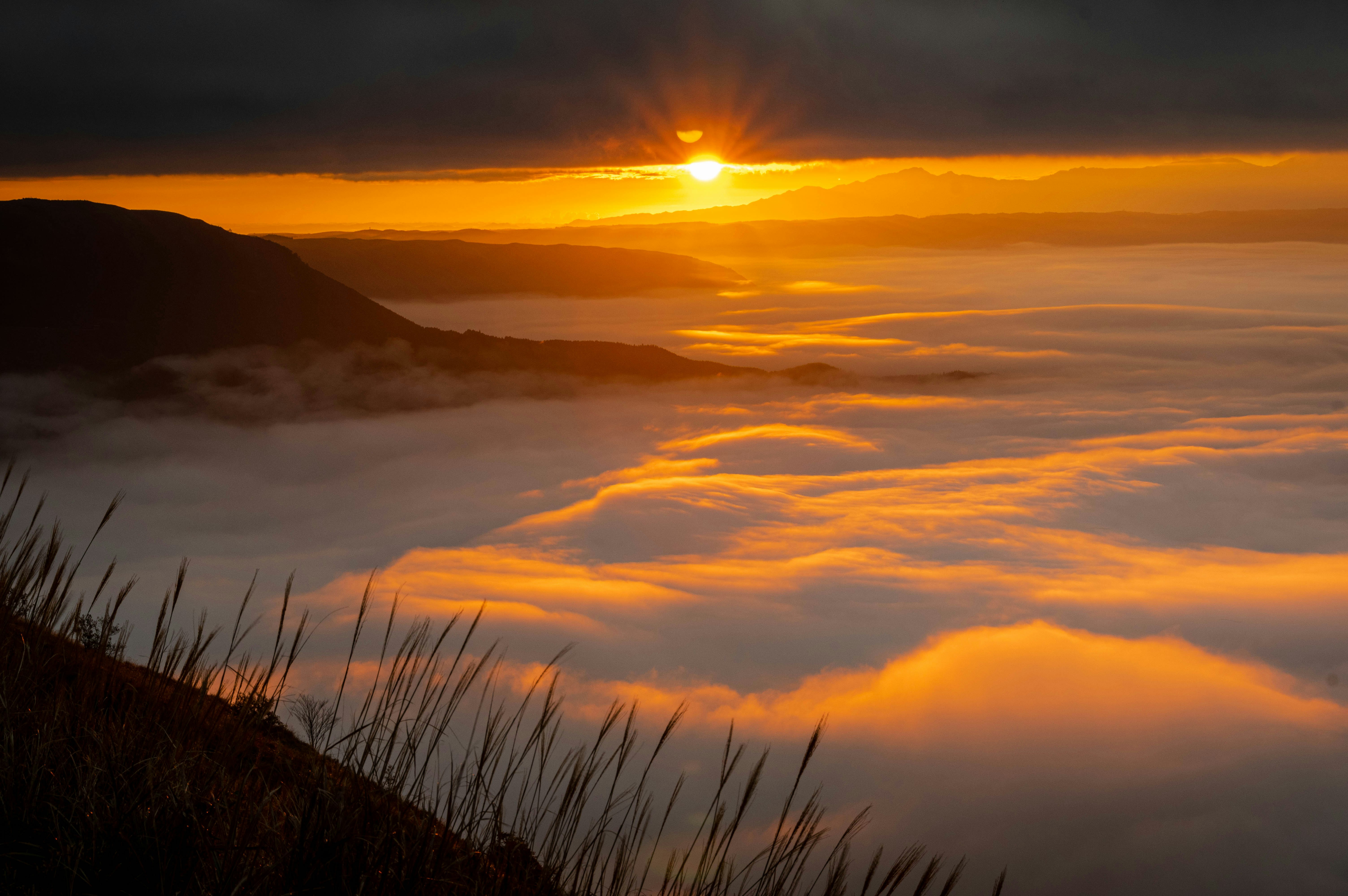 Coucher de soleil sur une mer de brume et des montagnes couvertes de nuages