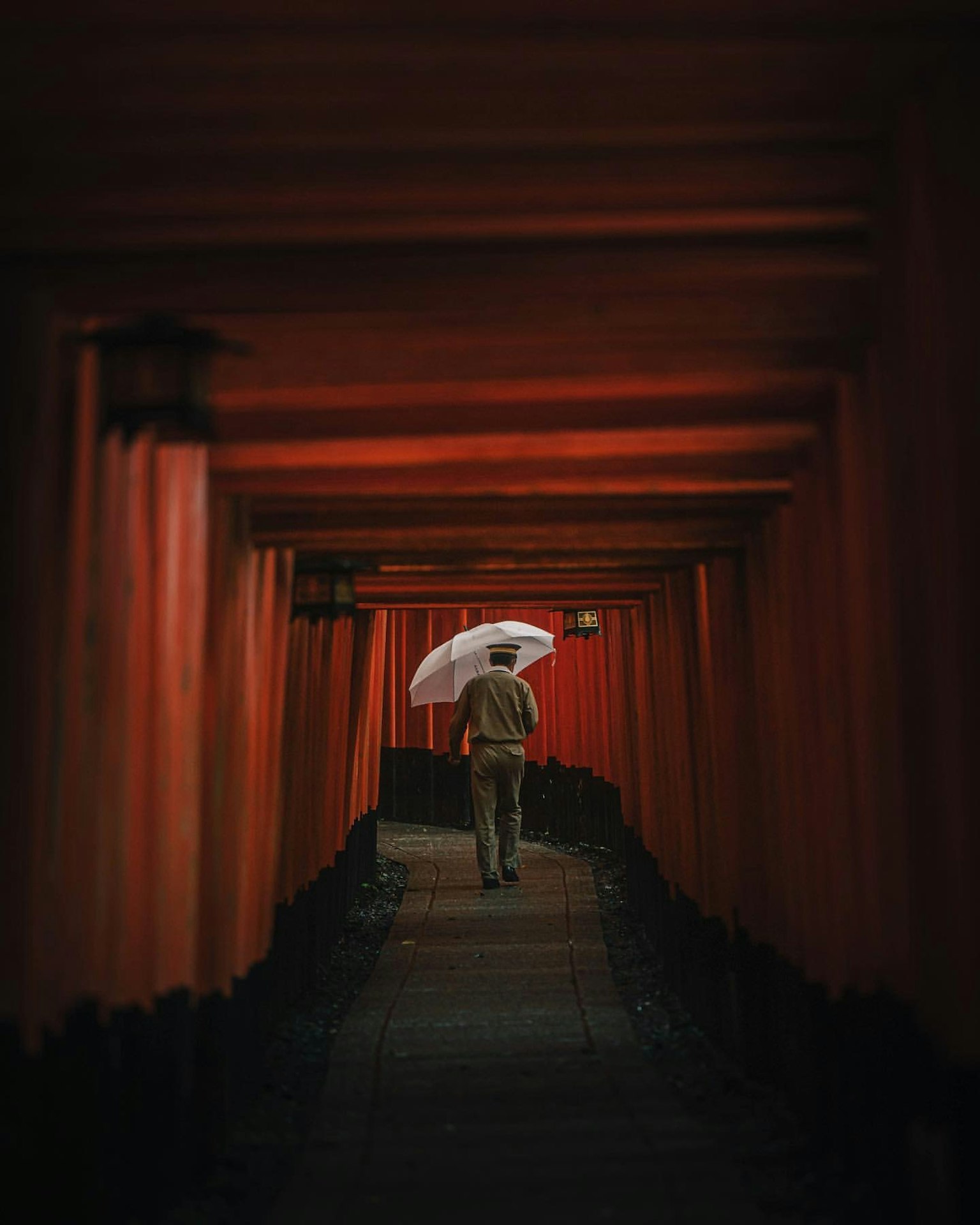 A person walking with an umbrella through red torii gates