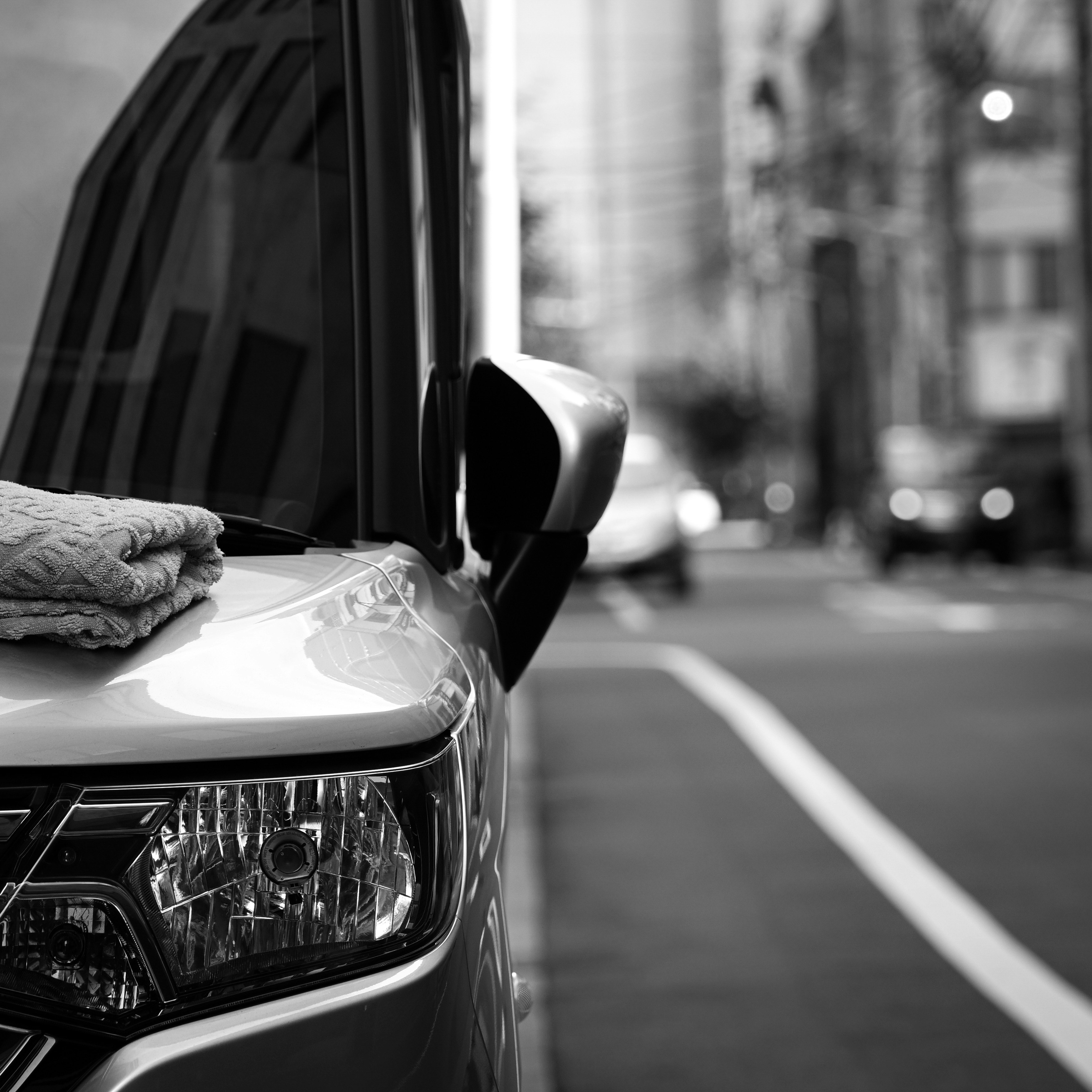 モノクロの路上で車のボンネットを洗う手元