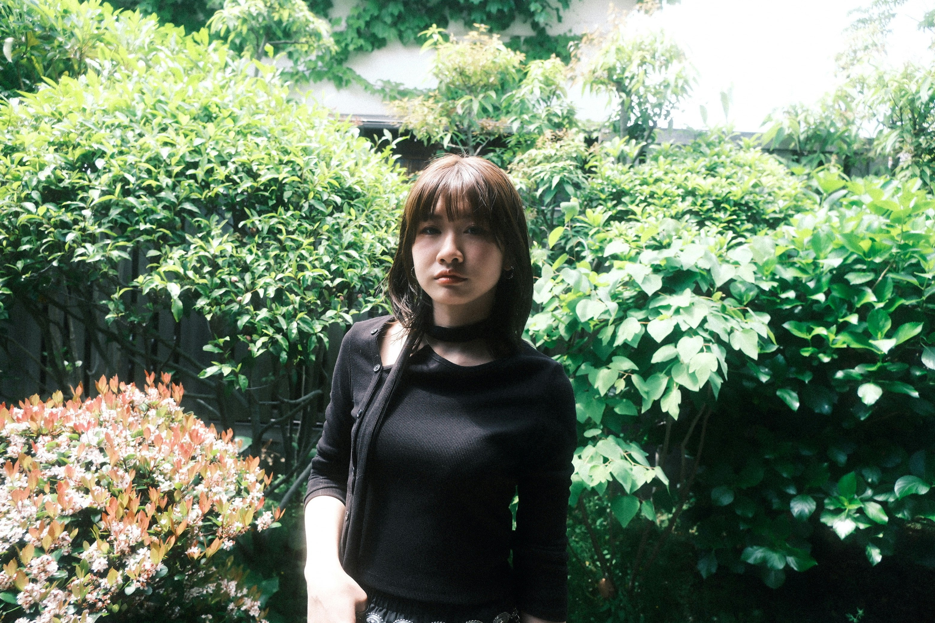 緑の生け垣に囲まれた花壇の前に立つ女性