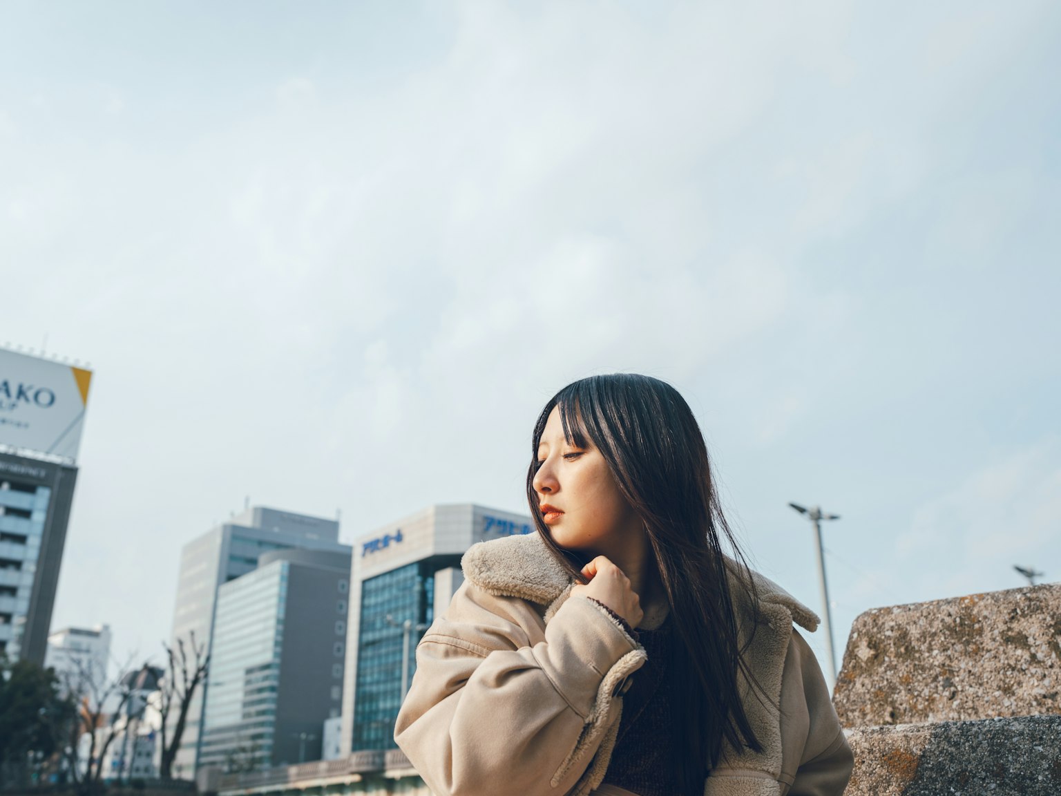 Una donna in cappotto che posa contro uno sfondo urbano con edifici moderni