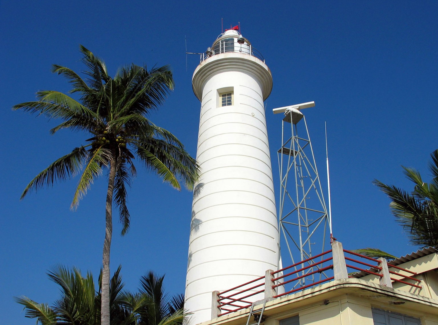 White lighthouse with palm trees against a blue sky