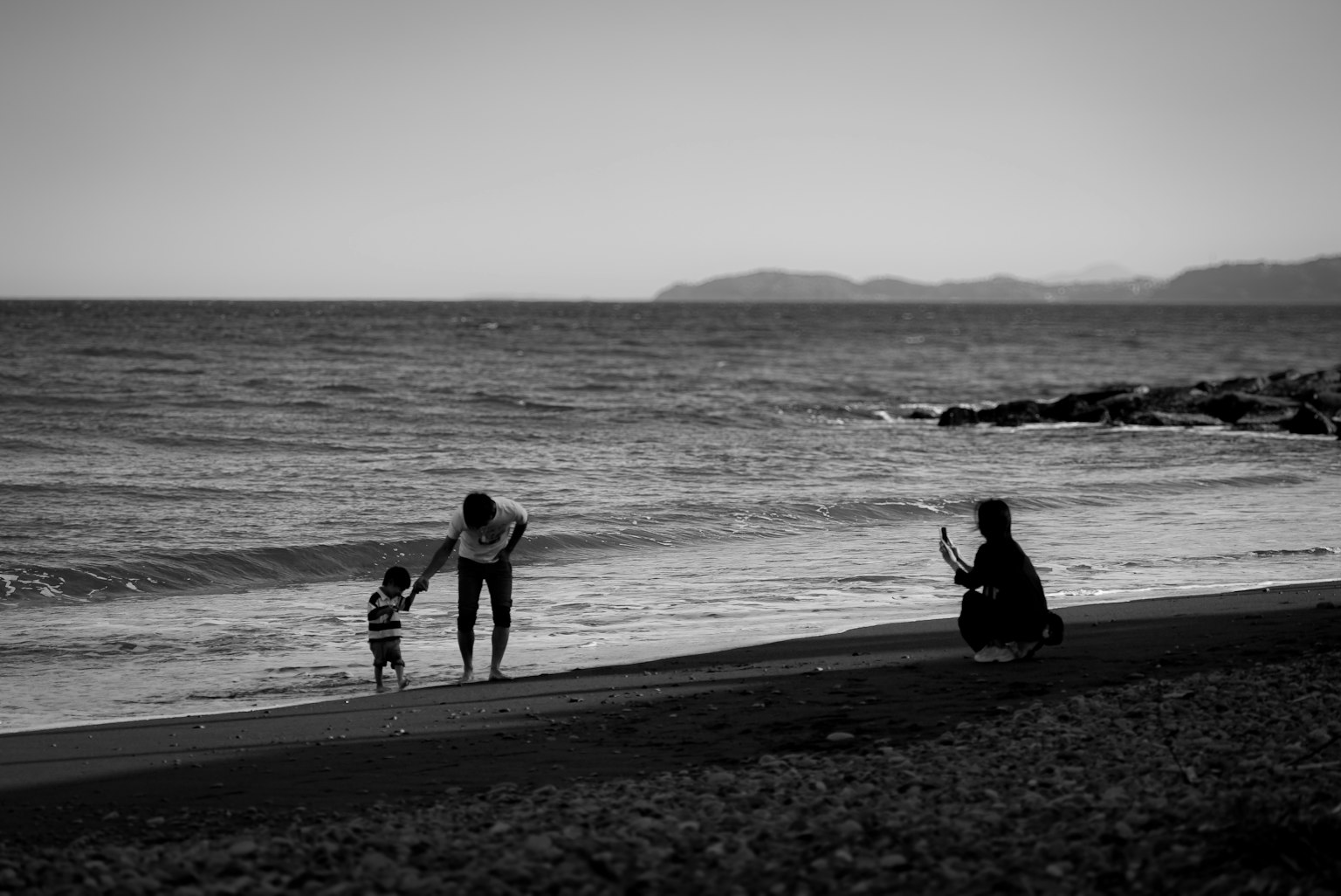 Silueta de un padre y un hijo jugando en la playa con una persona tomando una foto