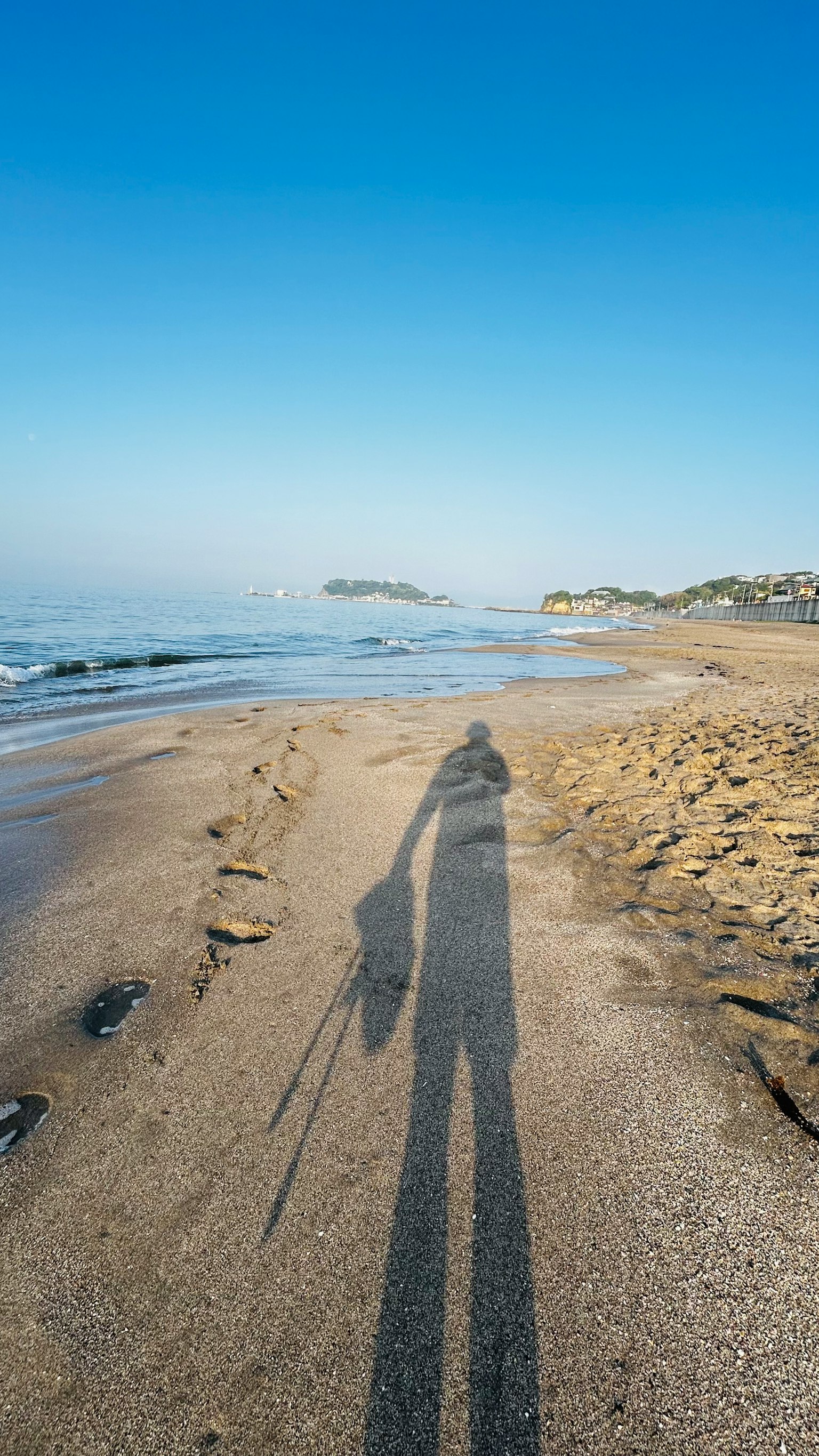 Shadow of a person walking along a beach under a clear blue sky