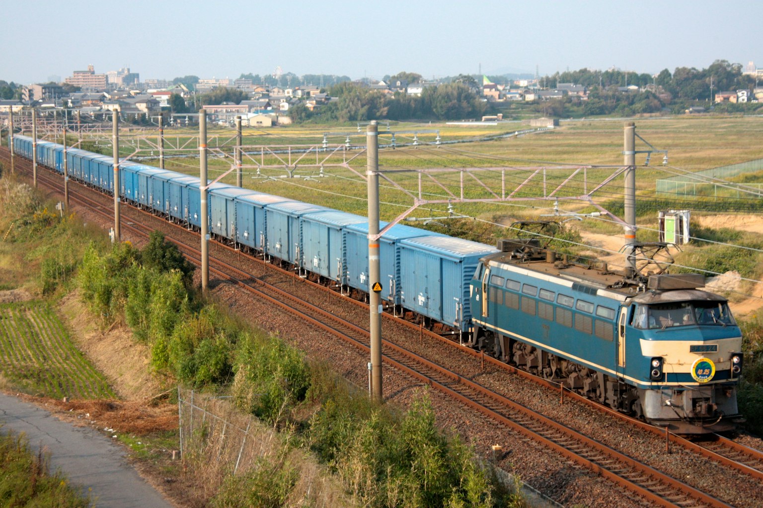 Un tren de carga azul viajando por las vías en un paisaje rural