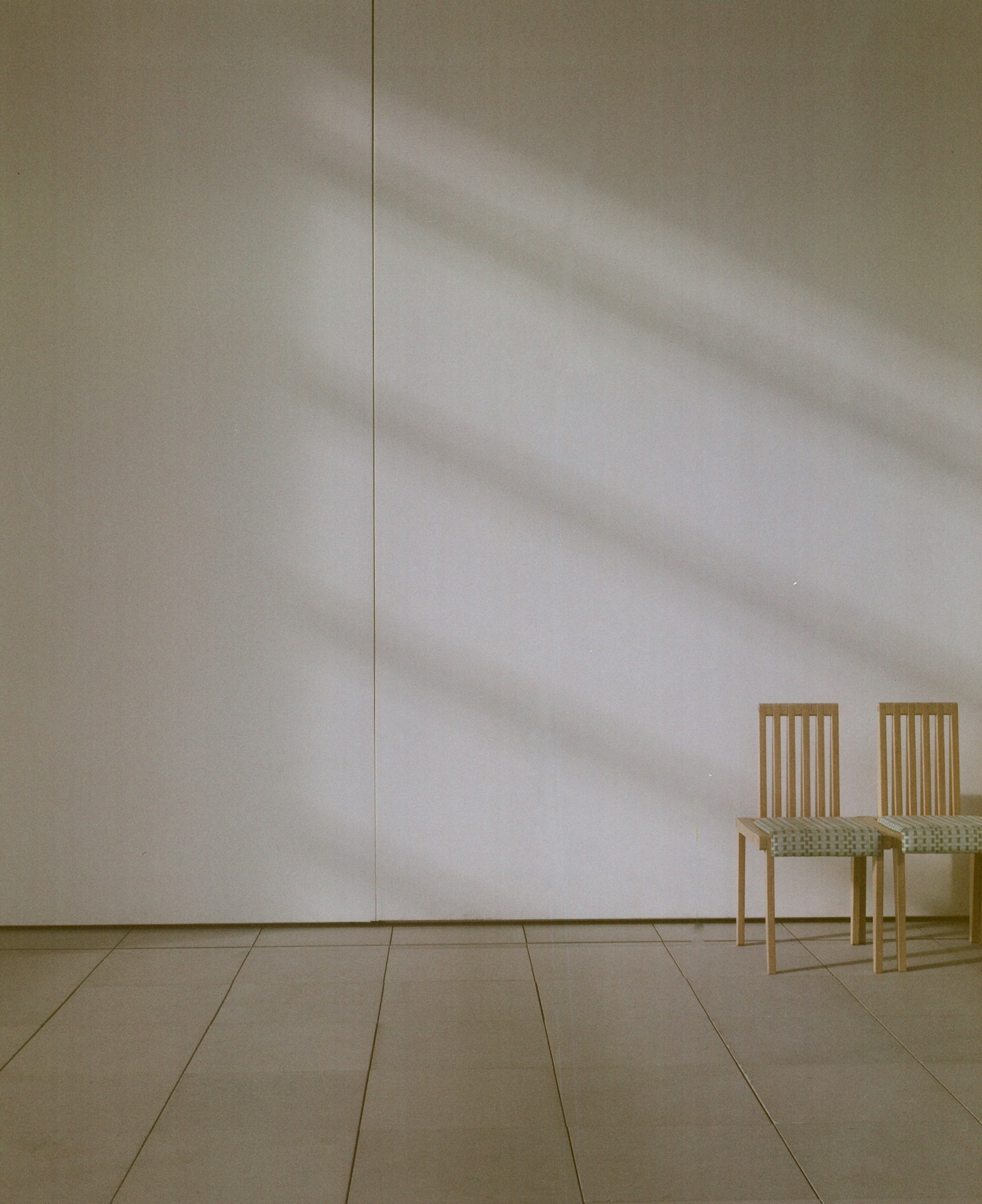 Sebuah interior minimalis dengan dinding putih dan dua kursi kayu