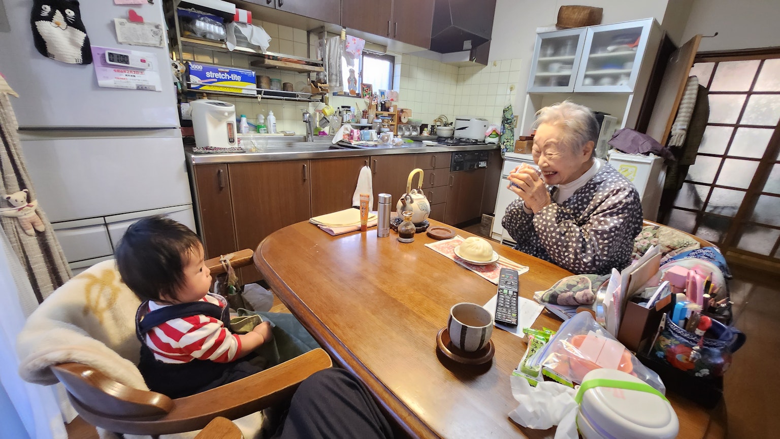 어린이와 노인이 아늑한 주방에서 나무 테이블에 앉아 식사를 즐기고 있는 장면