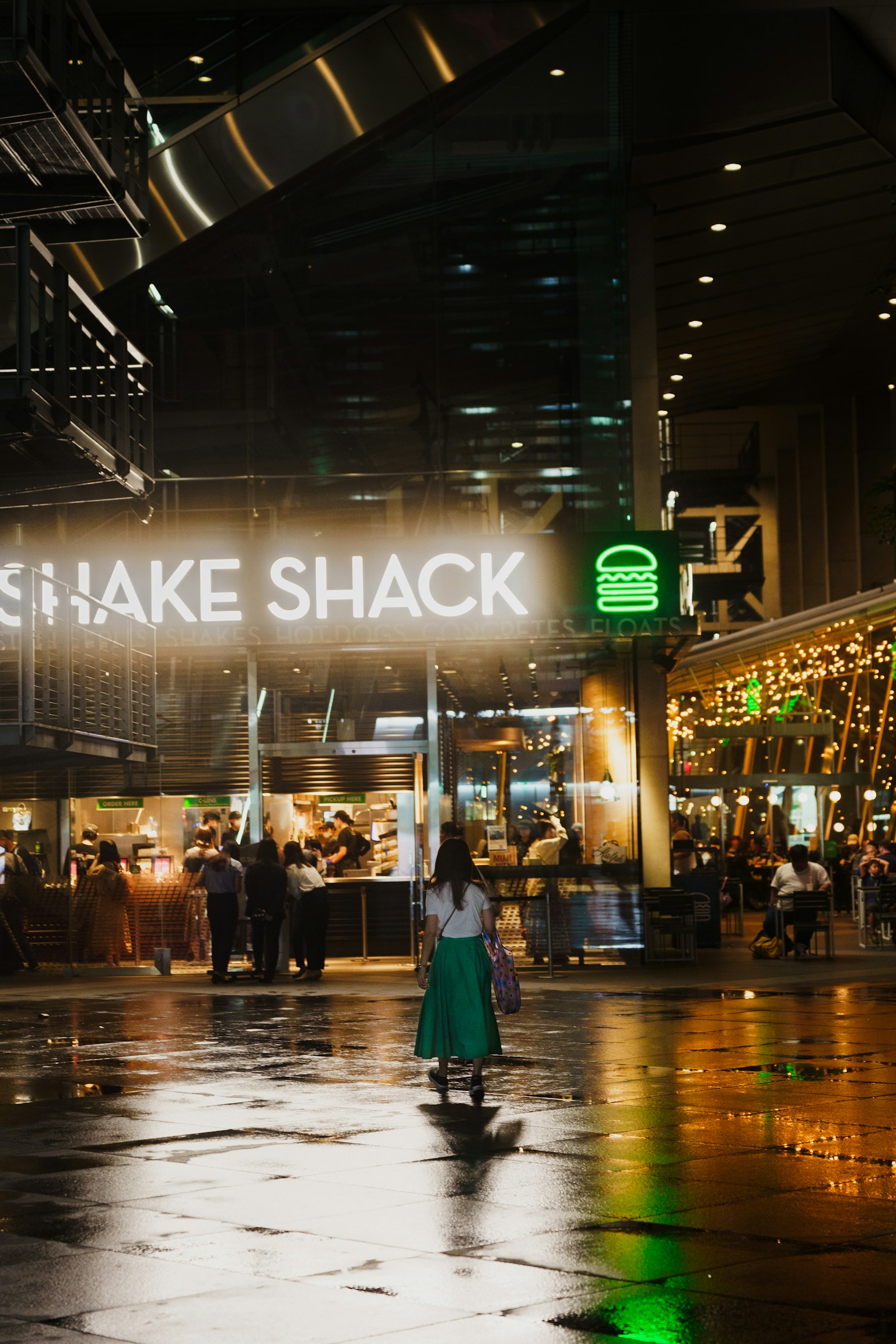 夜景中，閃耀的Shake Shack標誌在潮濕的人行道上反射