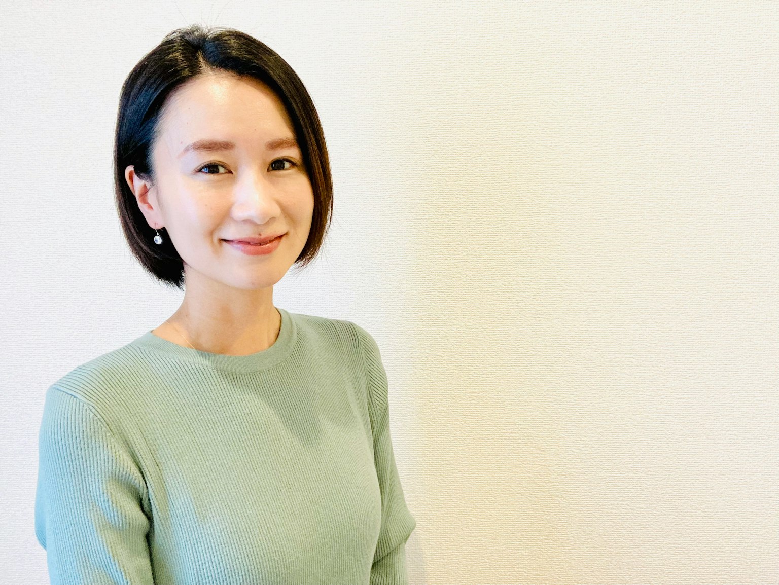 一位穿著淺綠色毛衣的女性微笑著，背景簡單
