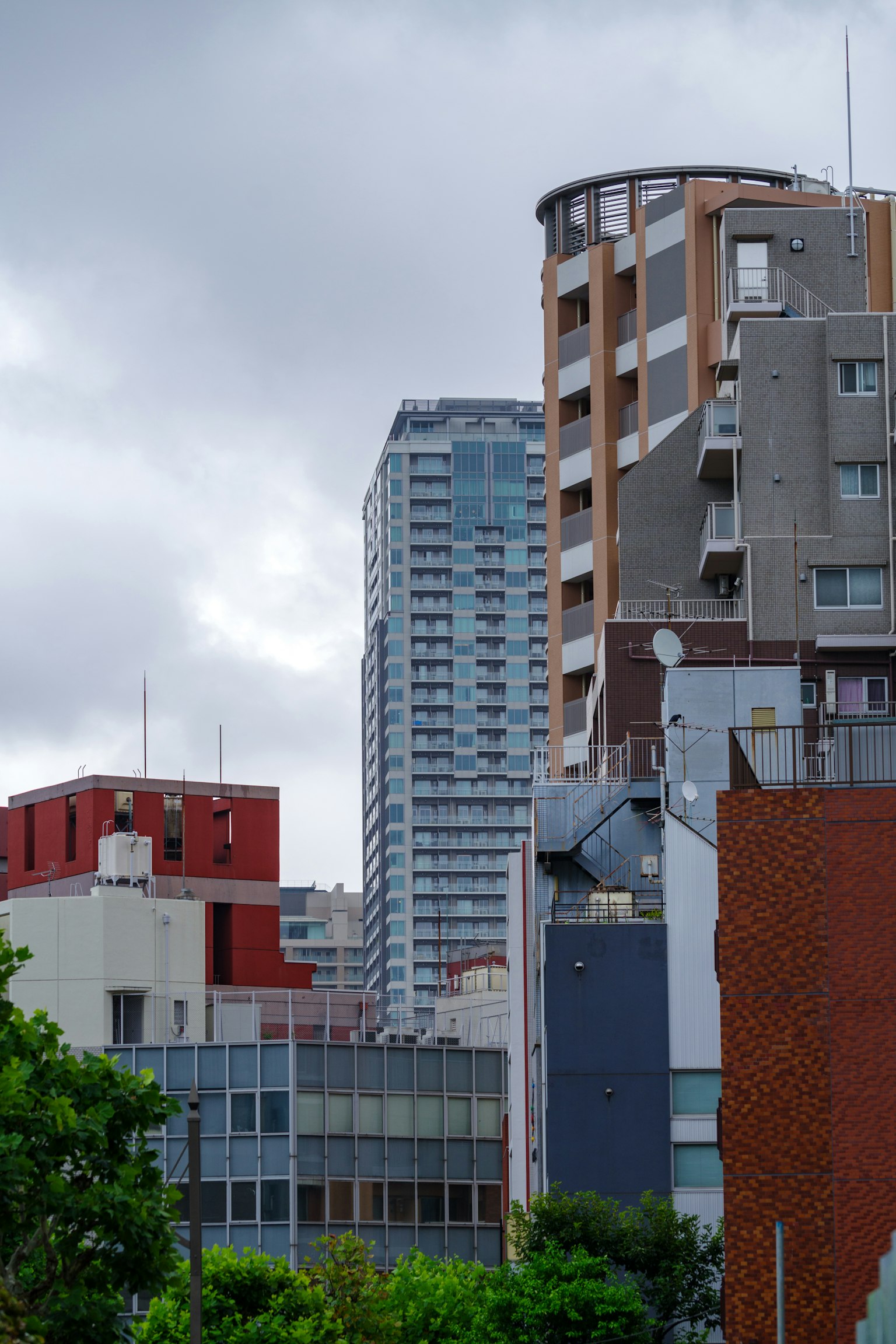 Urban landscape with high-rise and low-rise buildings under cloudy sky featuring green trees