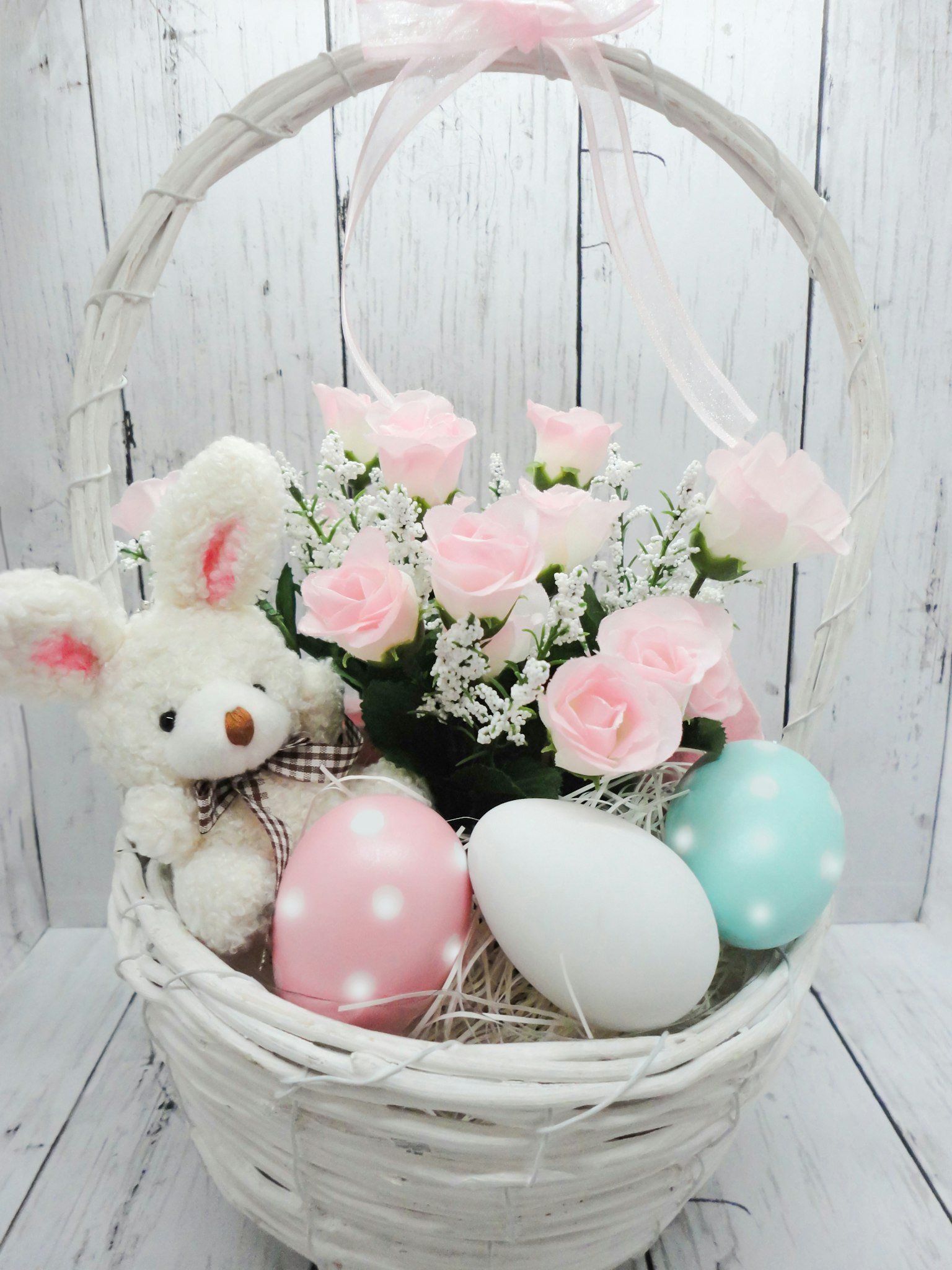 A white basket containing pink flowers and colorful eggs