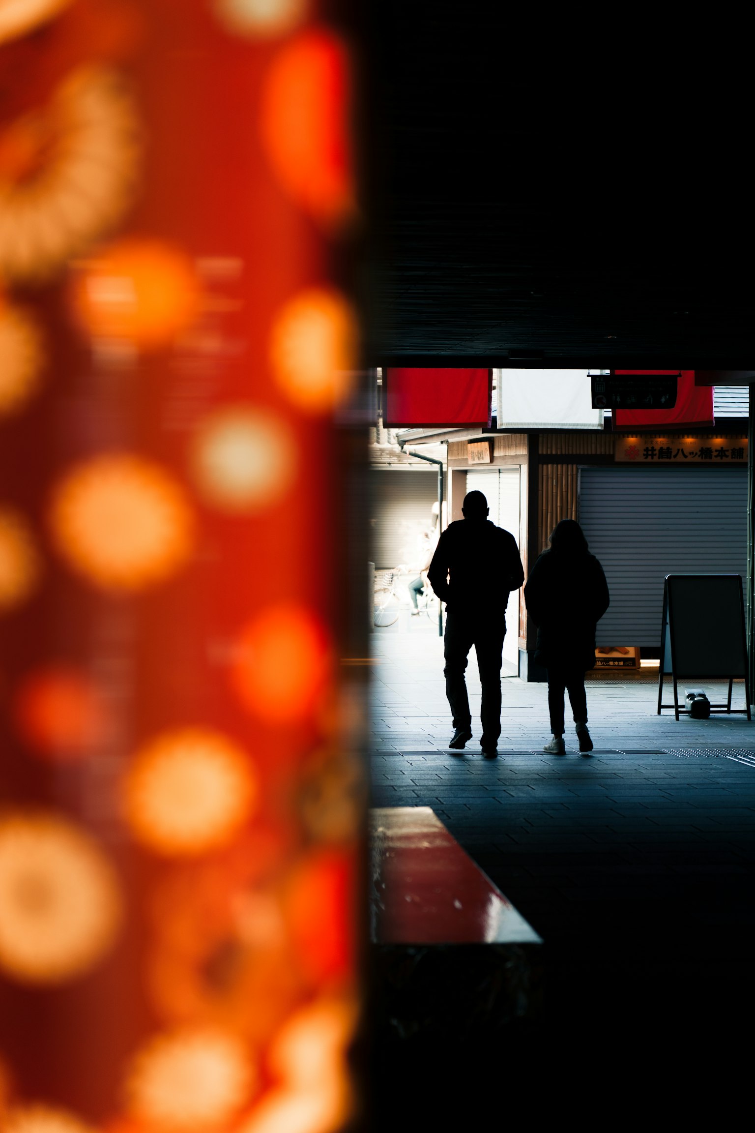 Silhouetten von zwei Personen, die hinter einem dekorativen roten Pfeiler in einem schwach beleuchteten Raum stehen