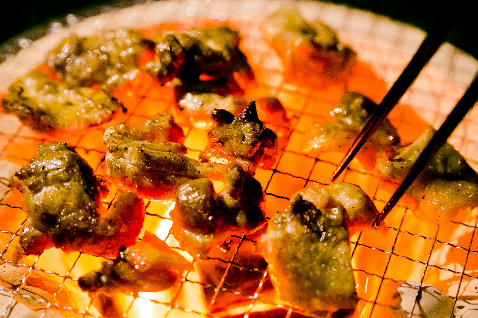 Grilled meat skewers on a charcoal grill with glowing embers