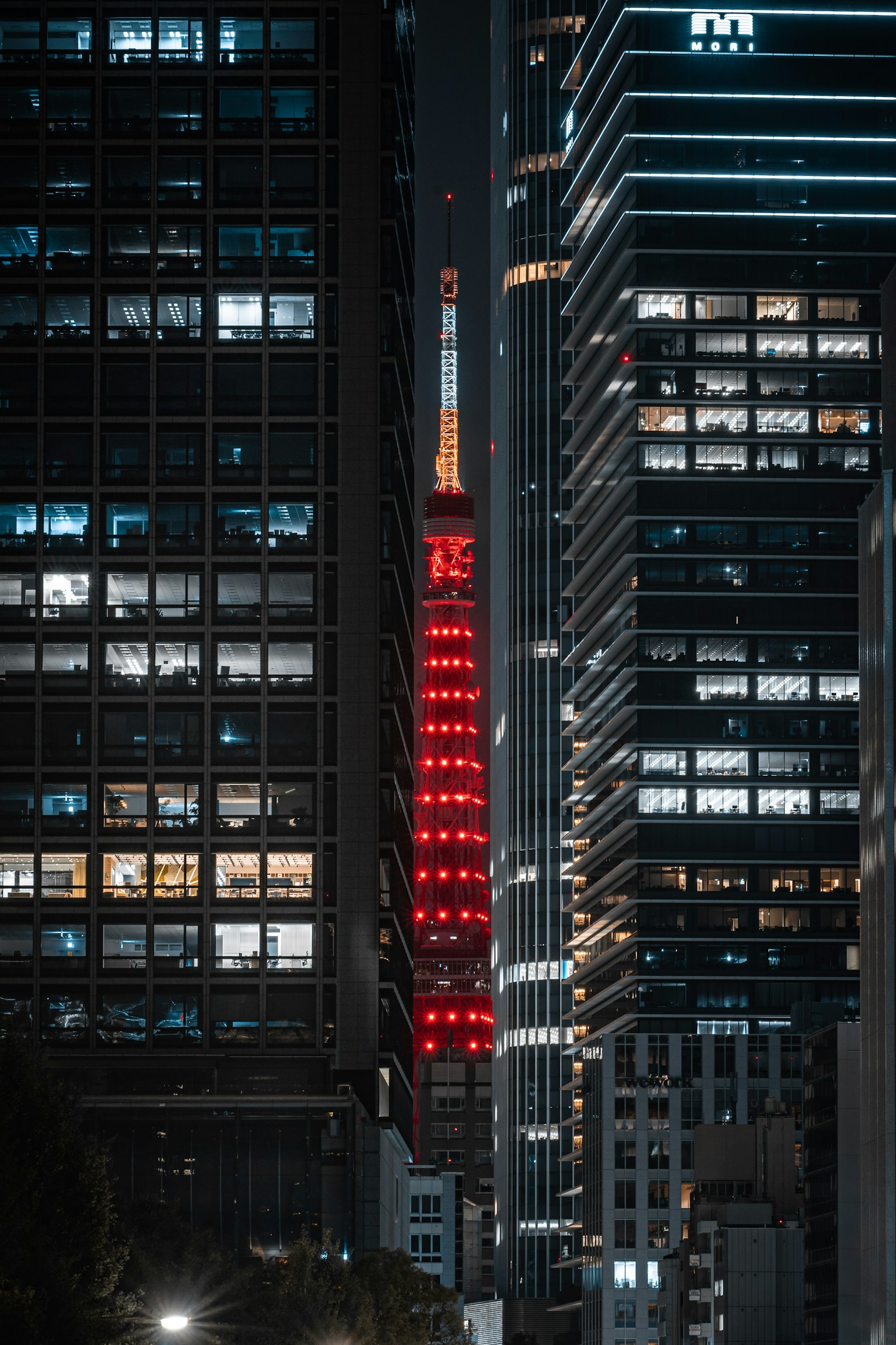 东京塔在夜间被红色灯光照亮，周围是摩天大楼