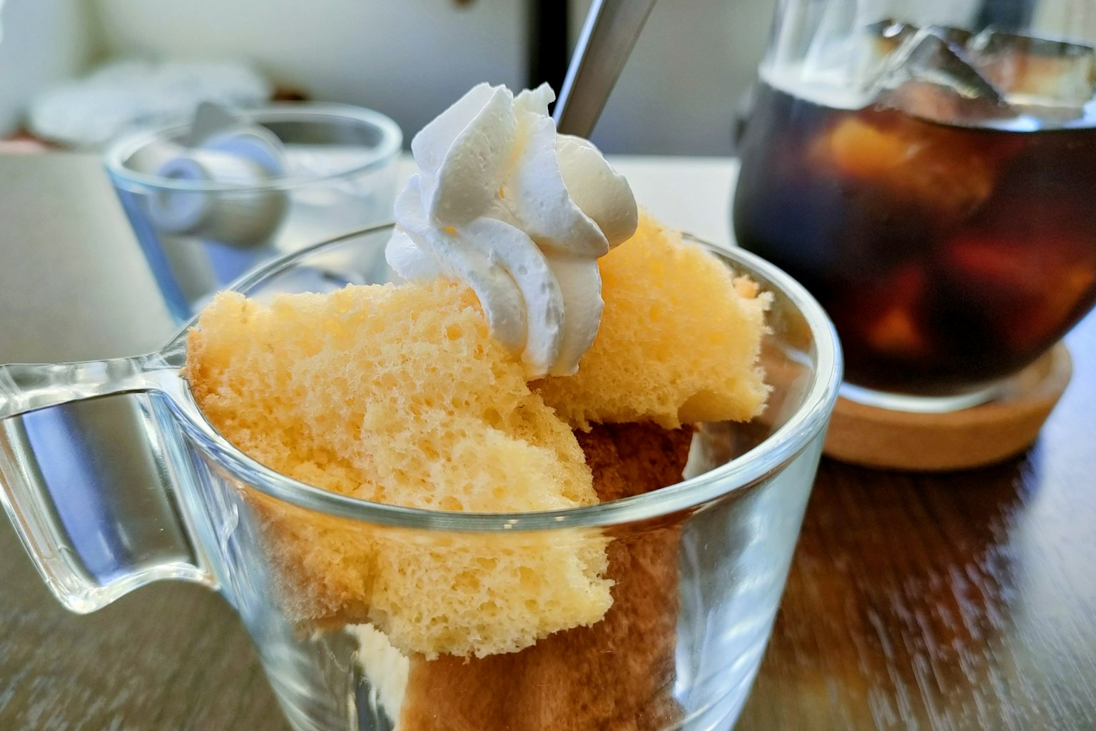 ขนมหวานในถ้วยที่มีเค้กฟองน้ำและครีมด้านบนพร้อมกับกาแฟเย็น