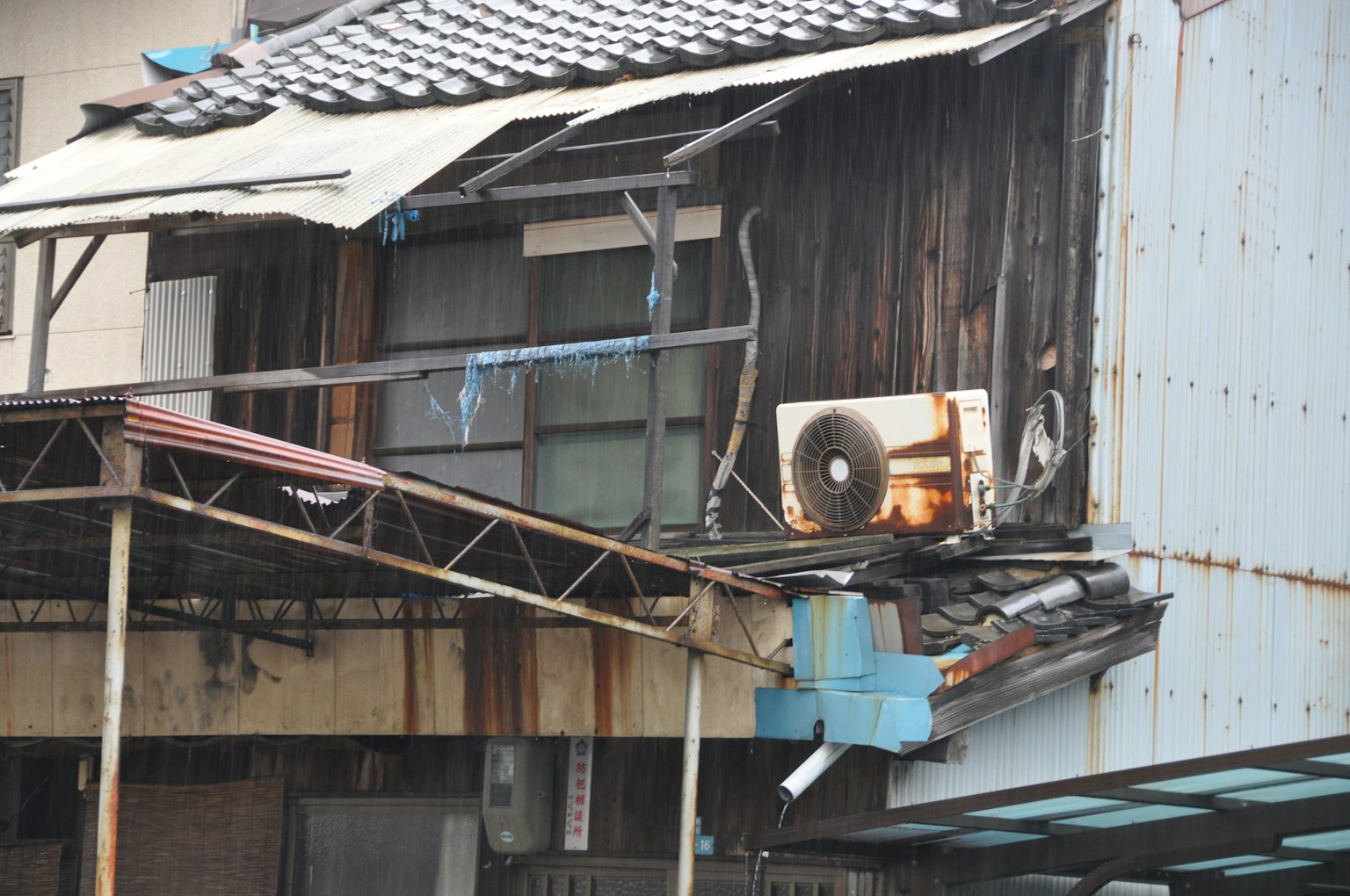 Eksterior gedung tua dengan kayu dan logam yang rusak serta unit pendingin udara