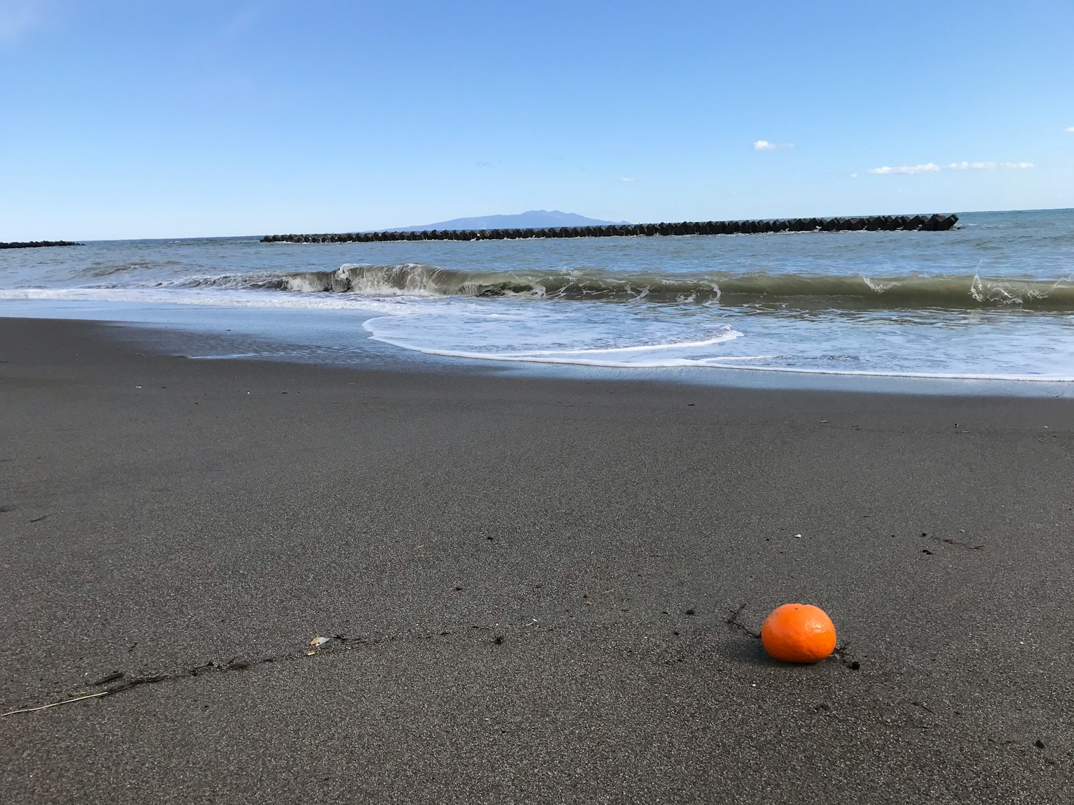 Sebuah bola oranye di pantai berpasir dengan ombak lembut