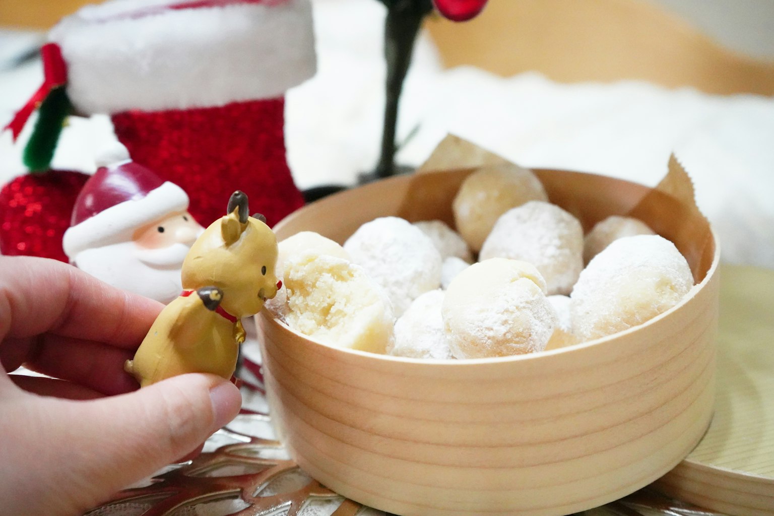 Tazón de madera lleno de golosinas espolvoreadas con azúcar glas junto a una pequeña figura de animal y decoraciones navideñas