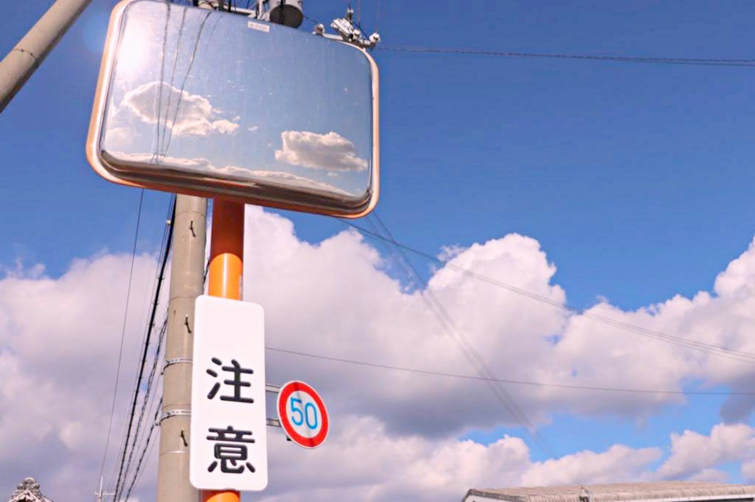 Verkehrsspiegel, der den blauen Himmel und Wolken reflektiert, mit Warnschild