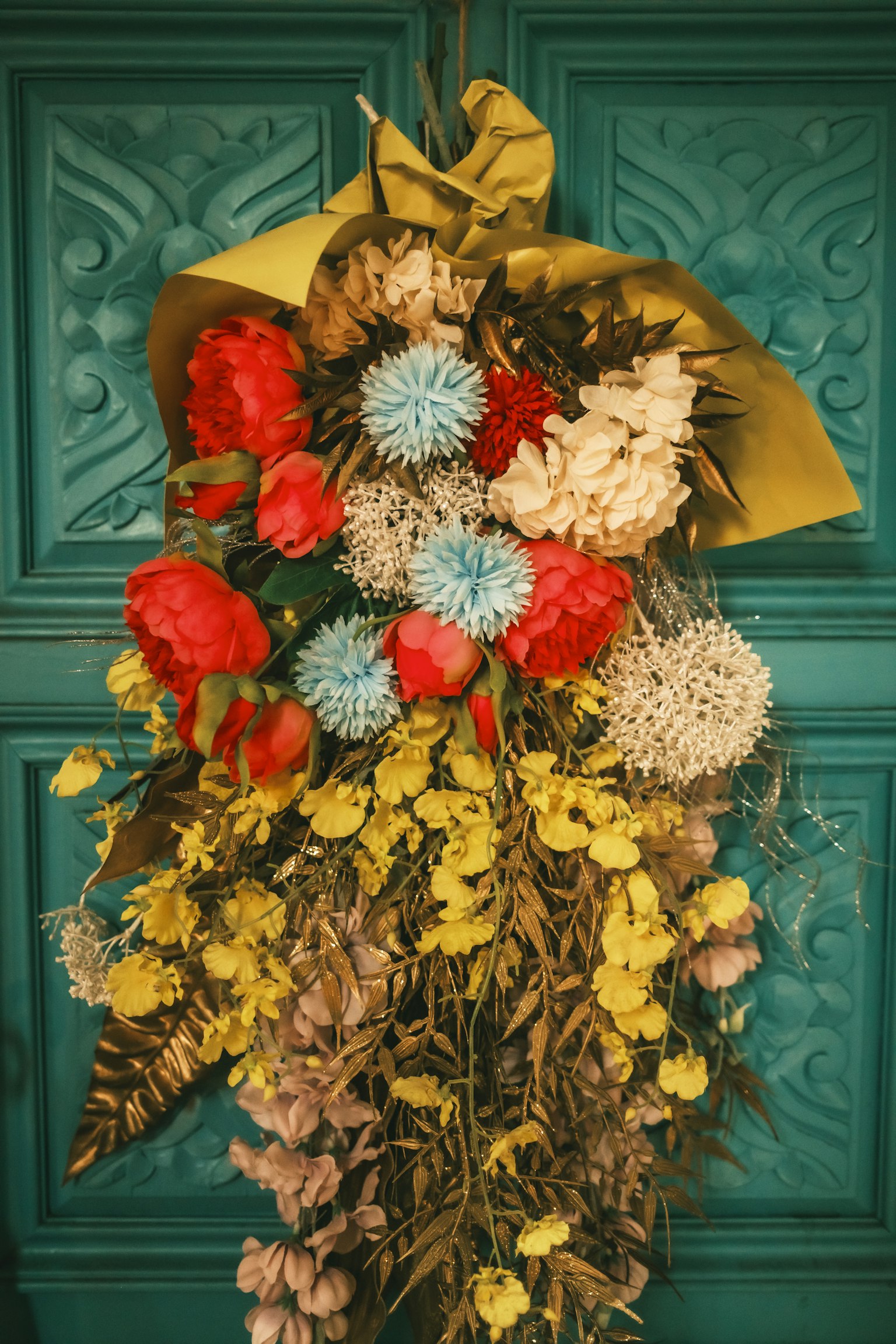 Arreglo de flores secas coloridas colgado en una puerta azul verdosa