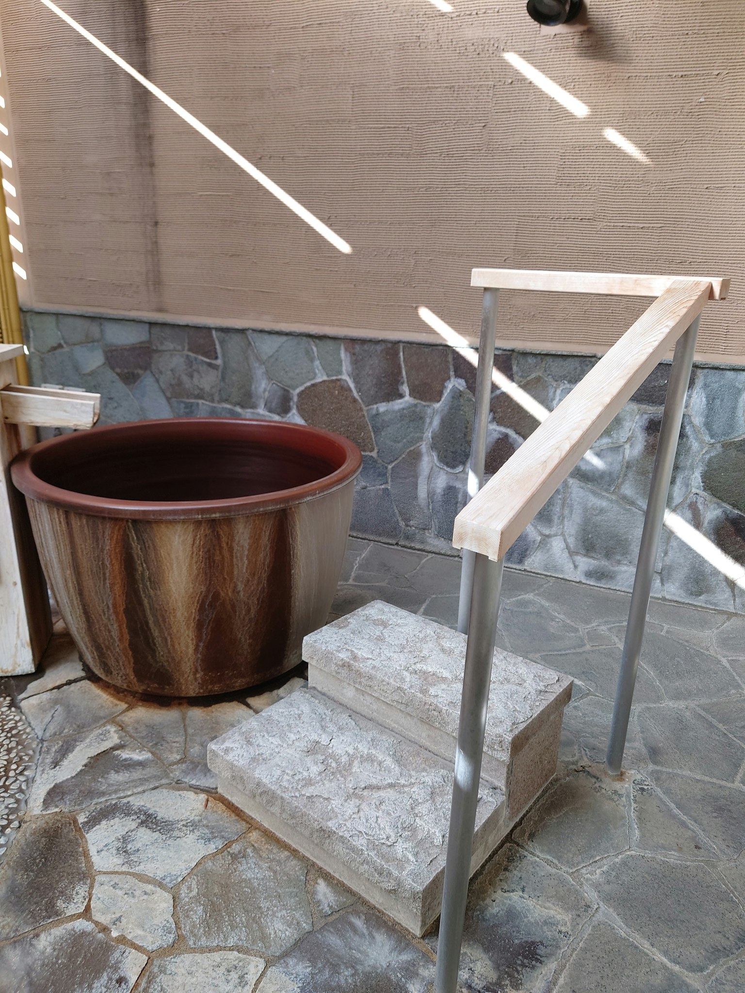 Escena al aire libre con escalones de madera y una barandilla de metal cerca de una gran tina