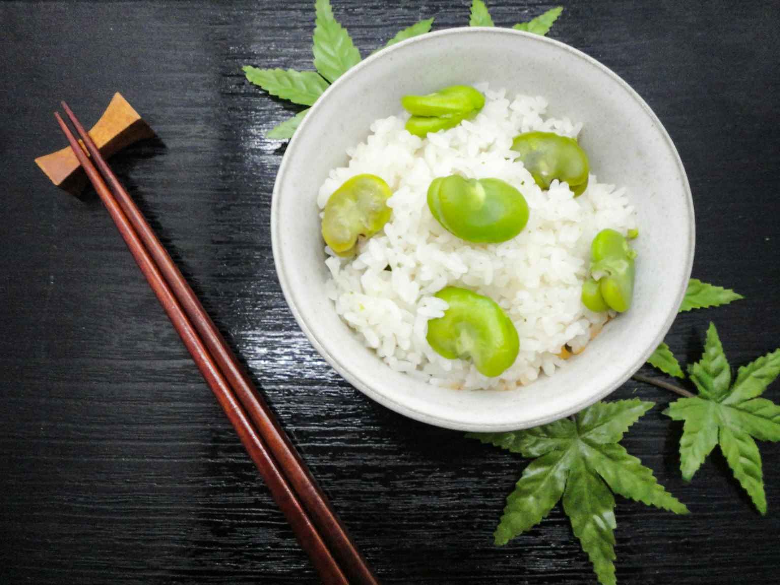 Bowl of white rice topped with fava beans placed on green leaves