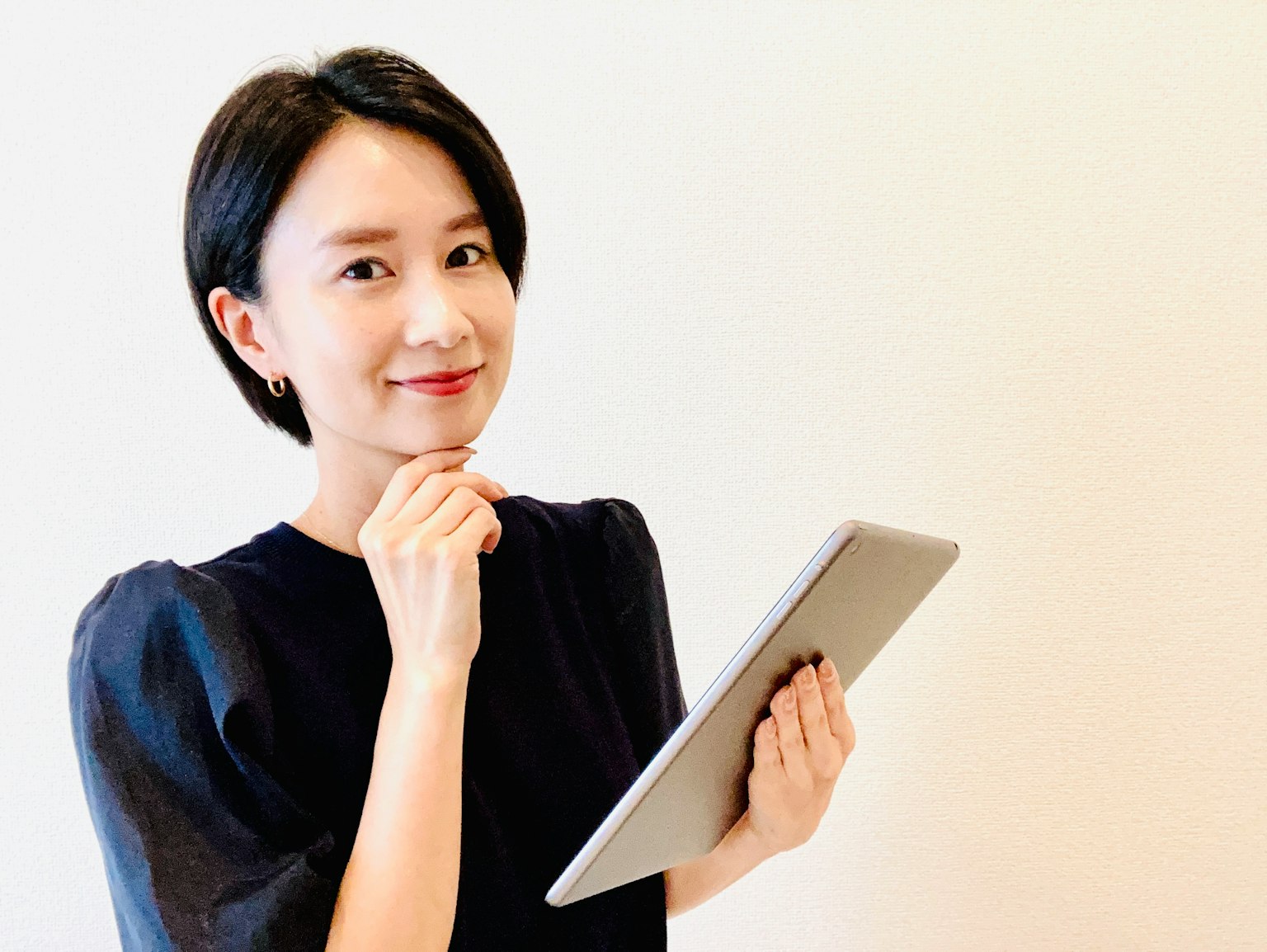 Một người phụ nữ cầm máy tính bảng và mỉm cười suy tư